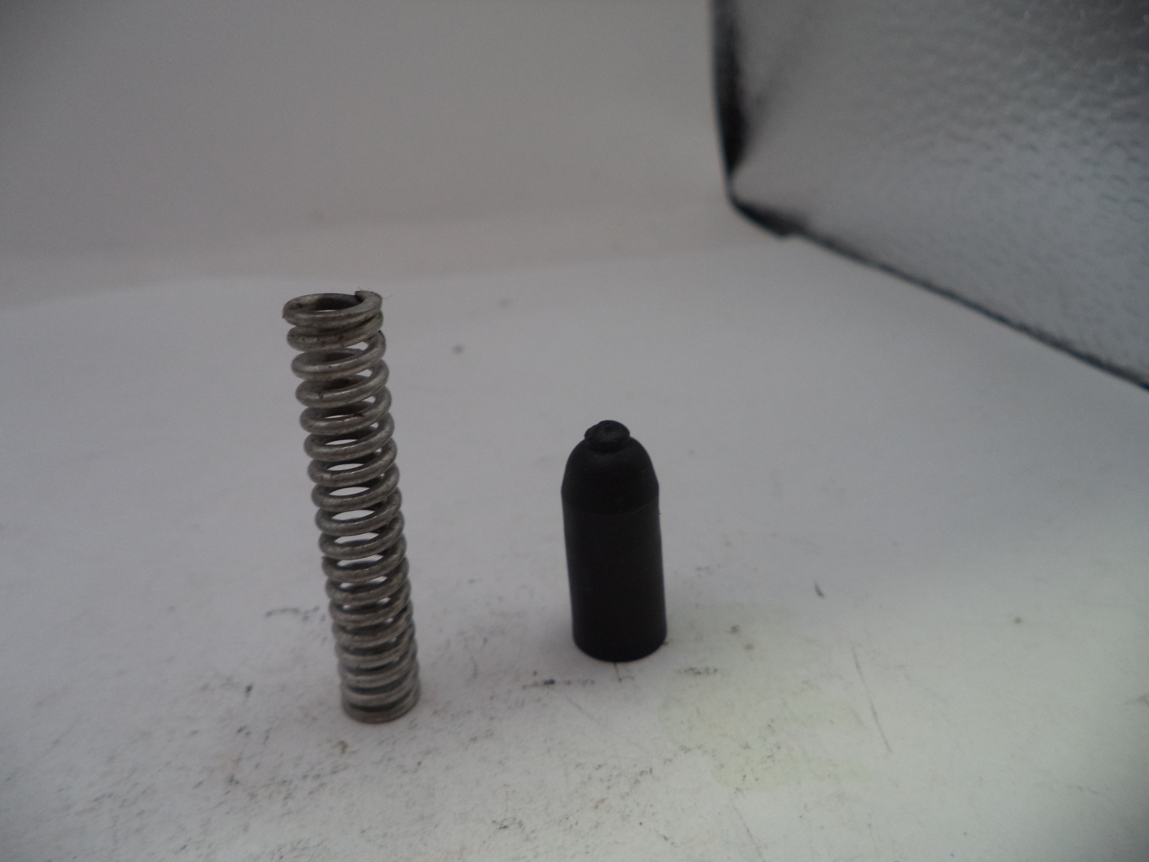 Metal spring and black cylindrical object on a white surface