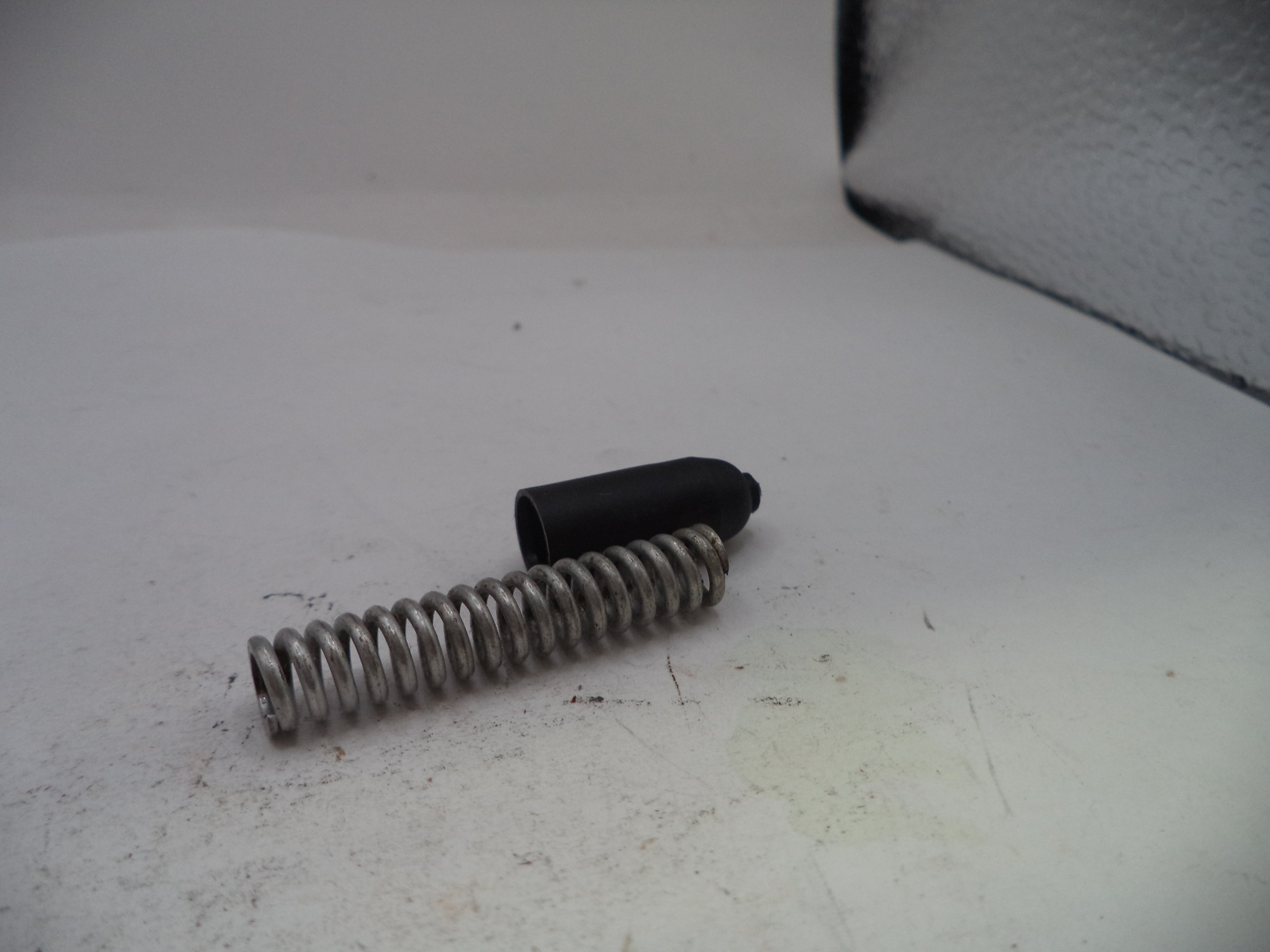 Metal spring and black cylindrical object on a white surface