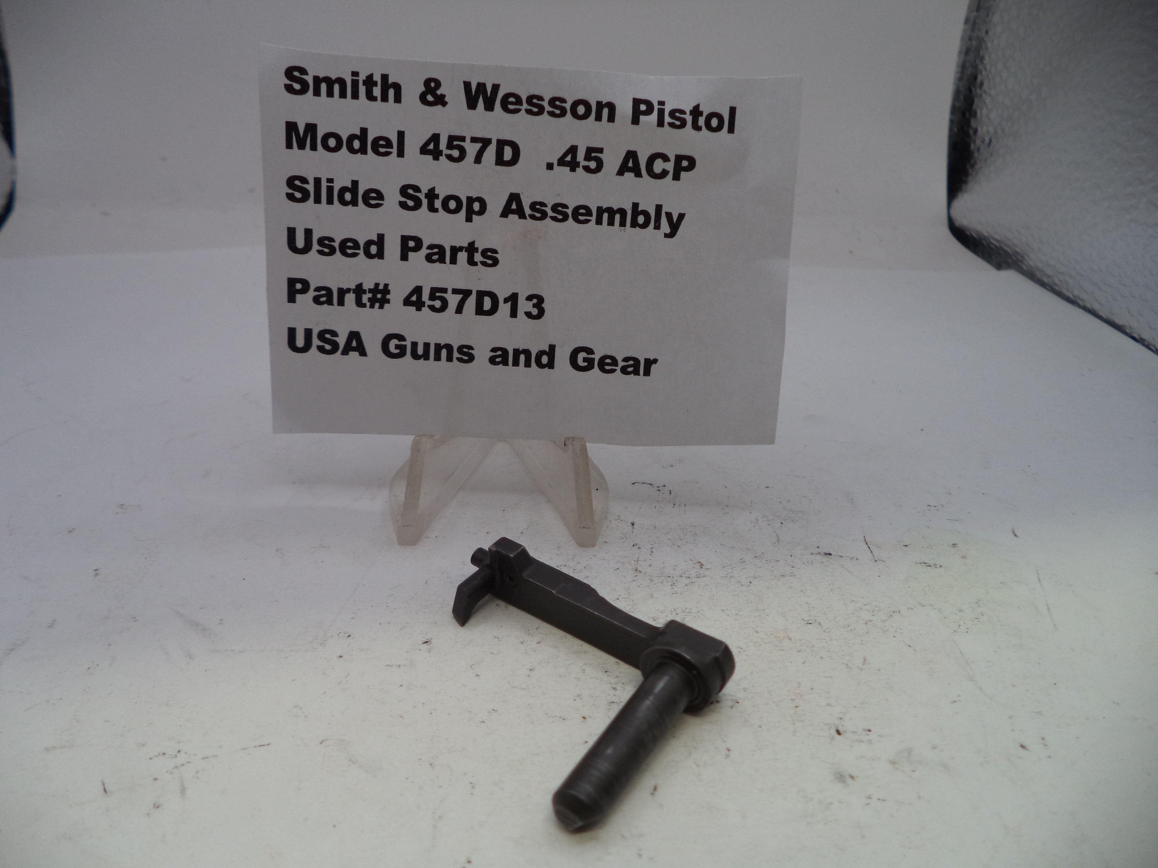 Smith & Wesson pistol slide stop assembly on a white surface with a label.