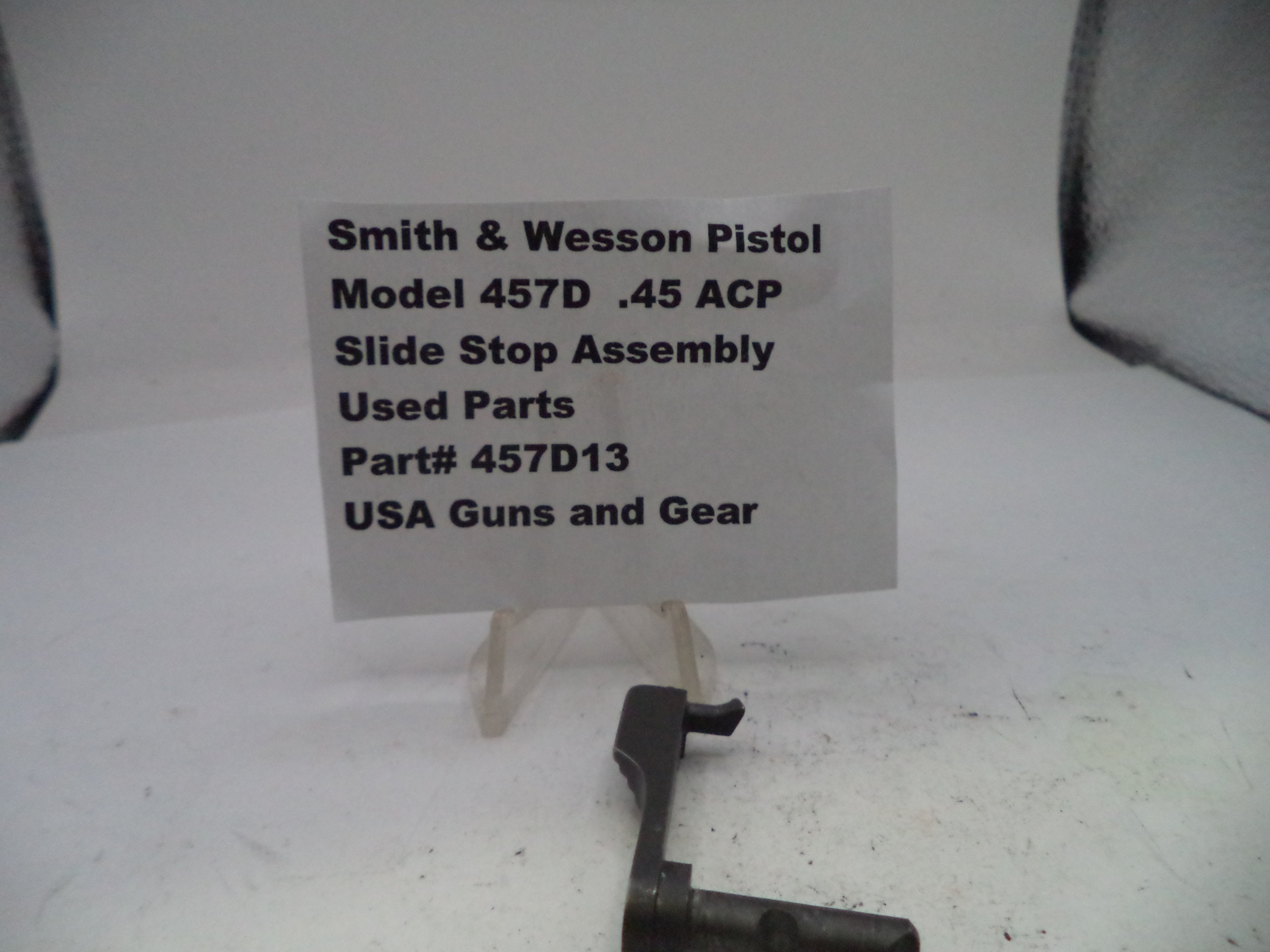 Smith & Wesson pistol slide stop assembly with a label on a white background
