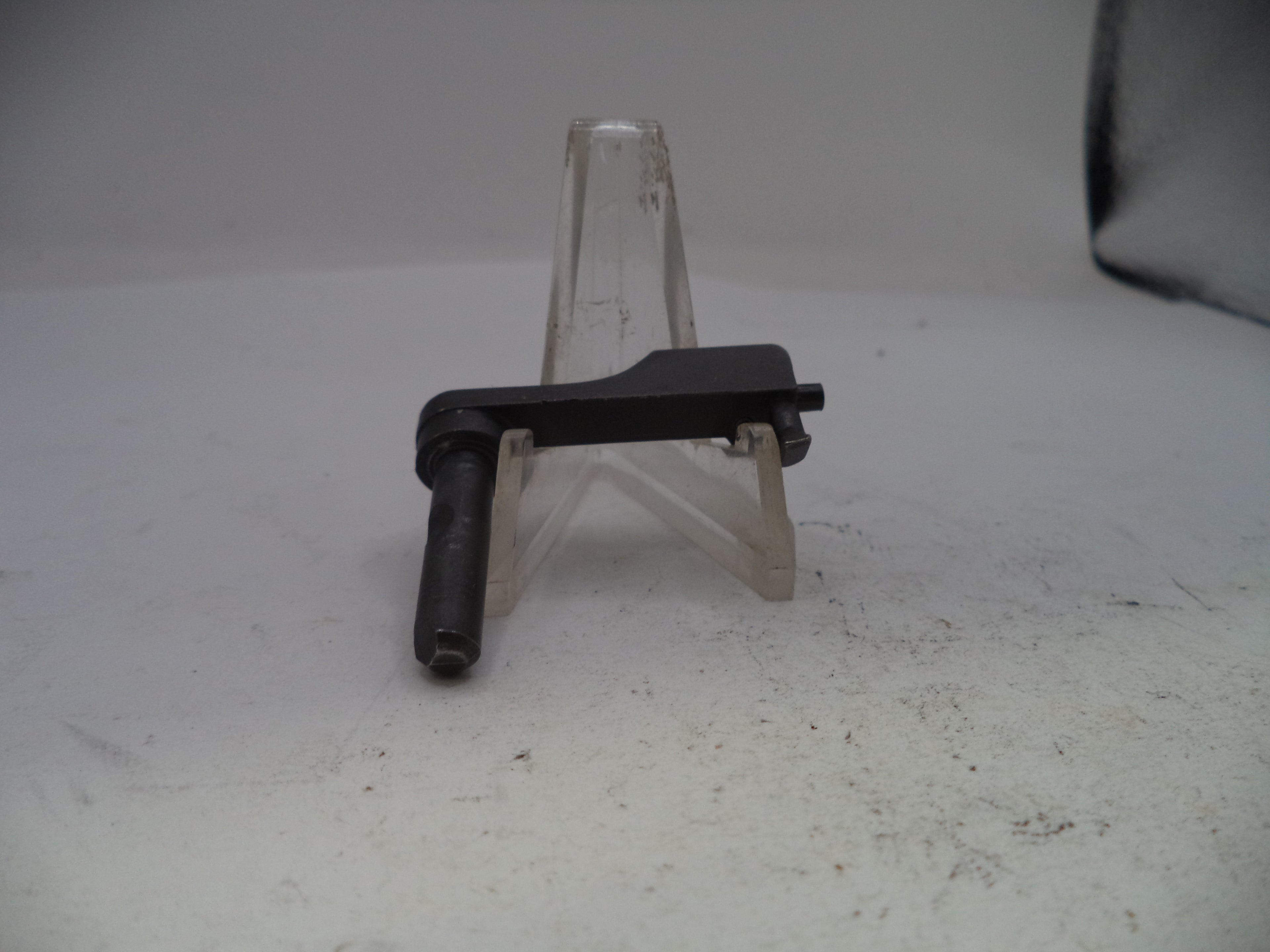 Small black metal component on a clear stand against a light gray background