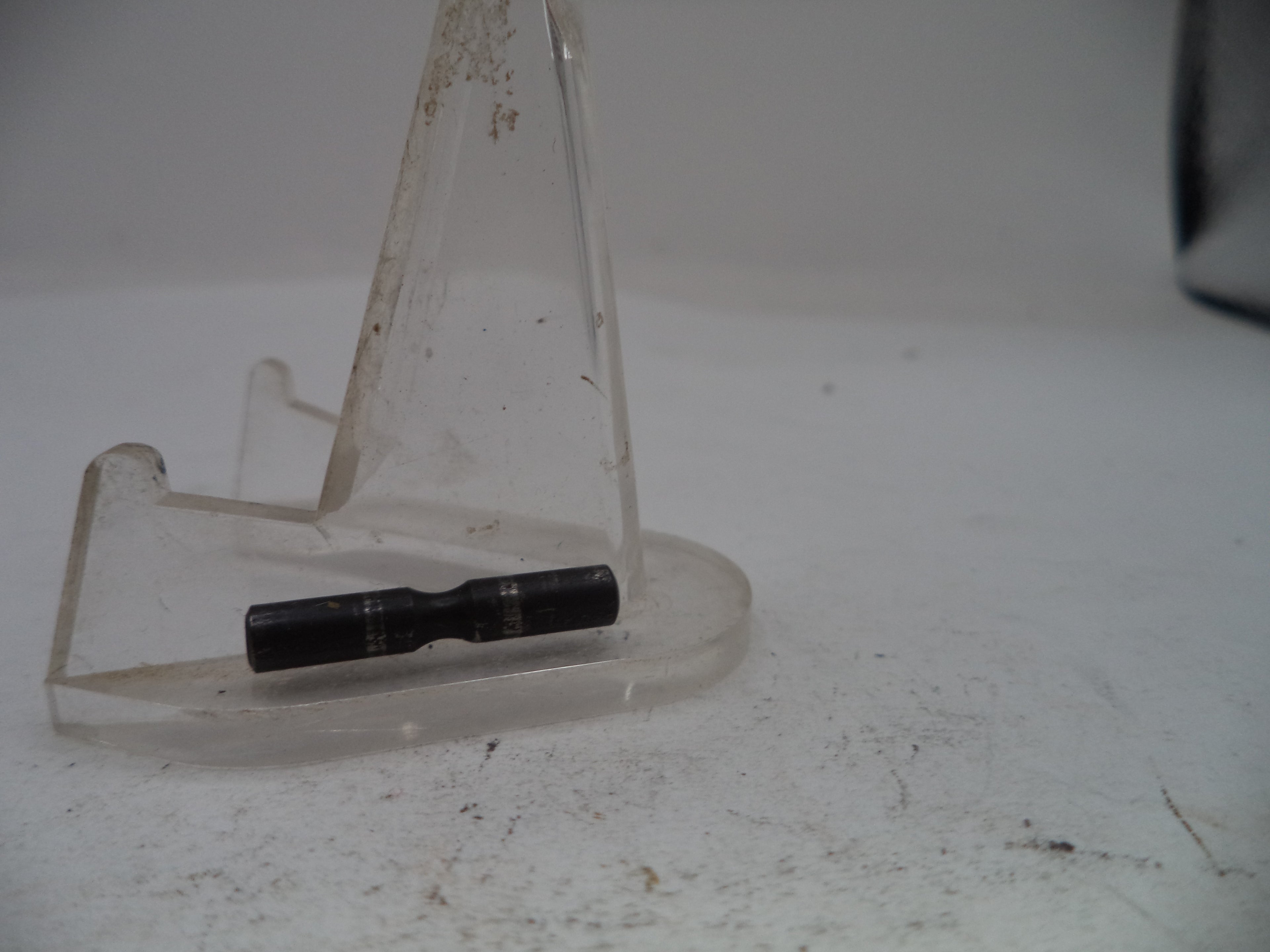 Black cylindrical object on a clear stand against a white background
