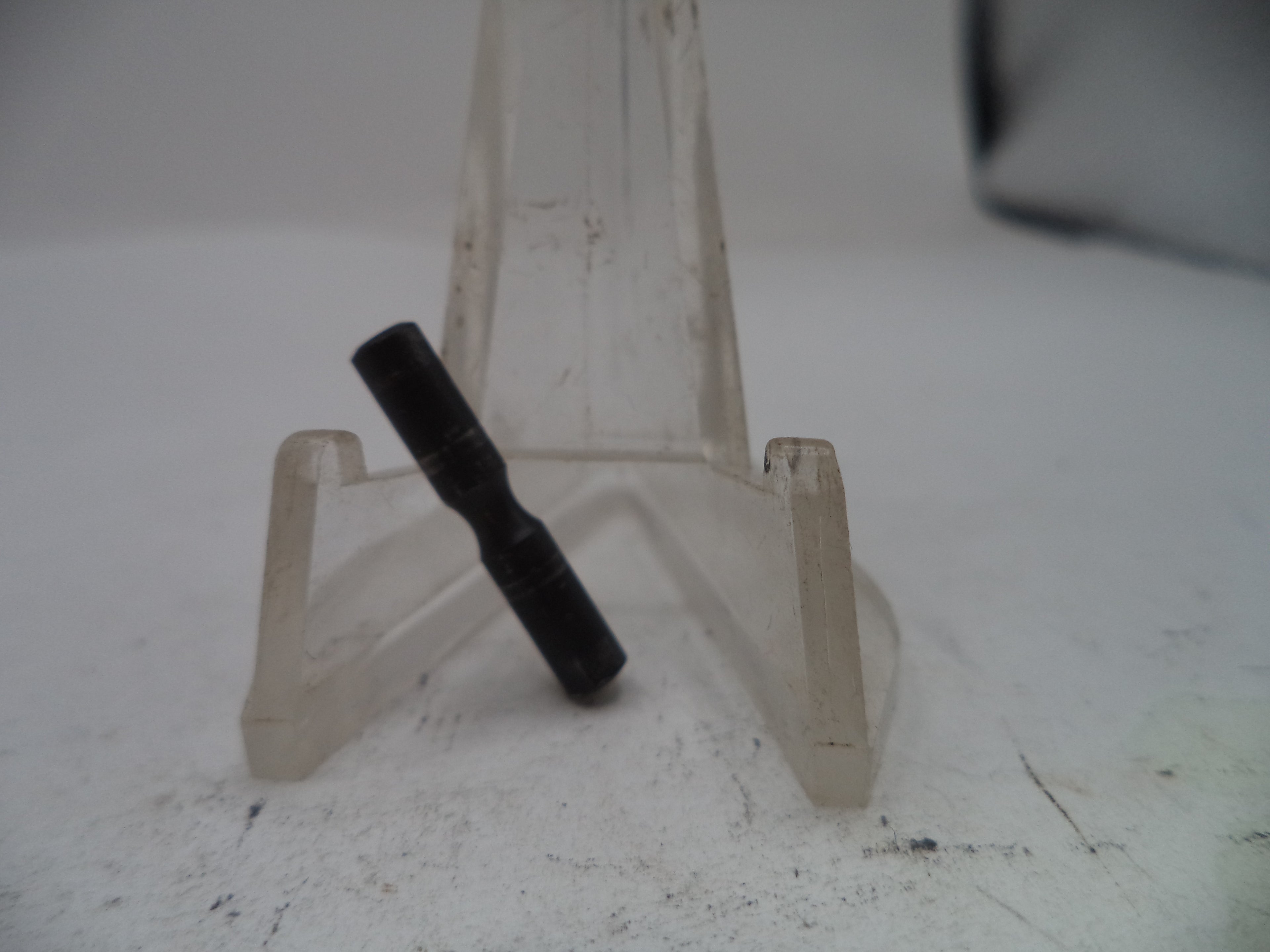Black cylindrical object on a clear plastic stand against a white background