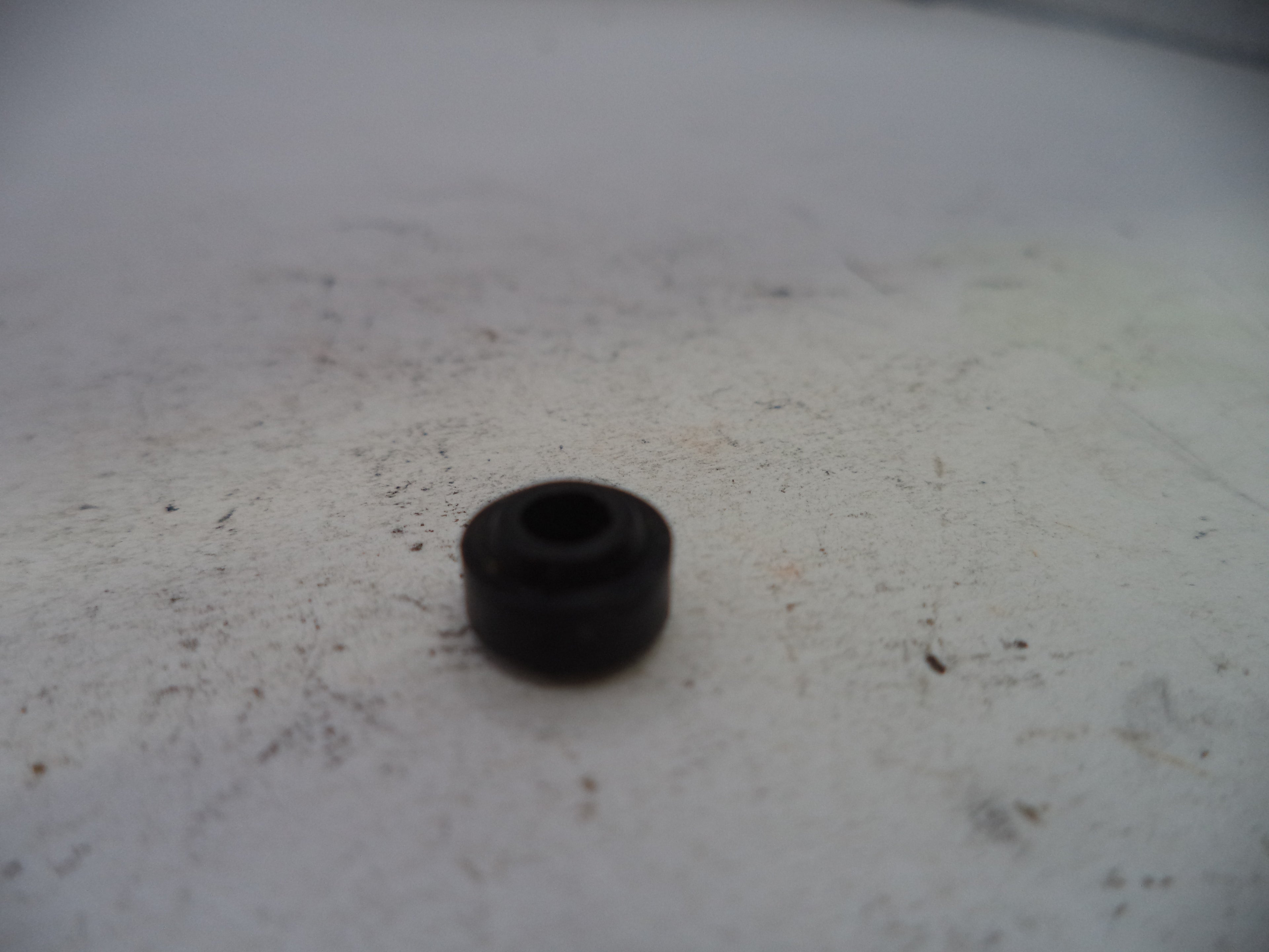 Small black rubber bushing on a white surface with visible dirt.