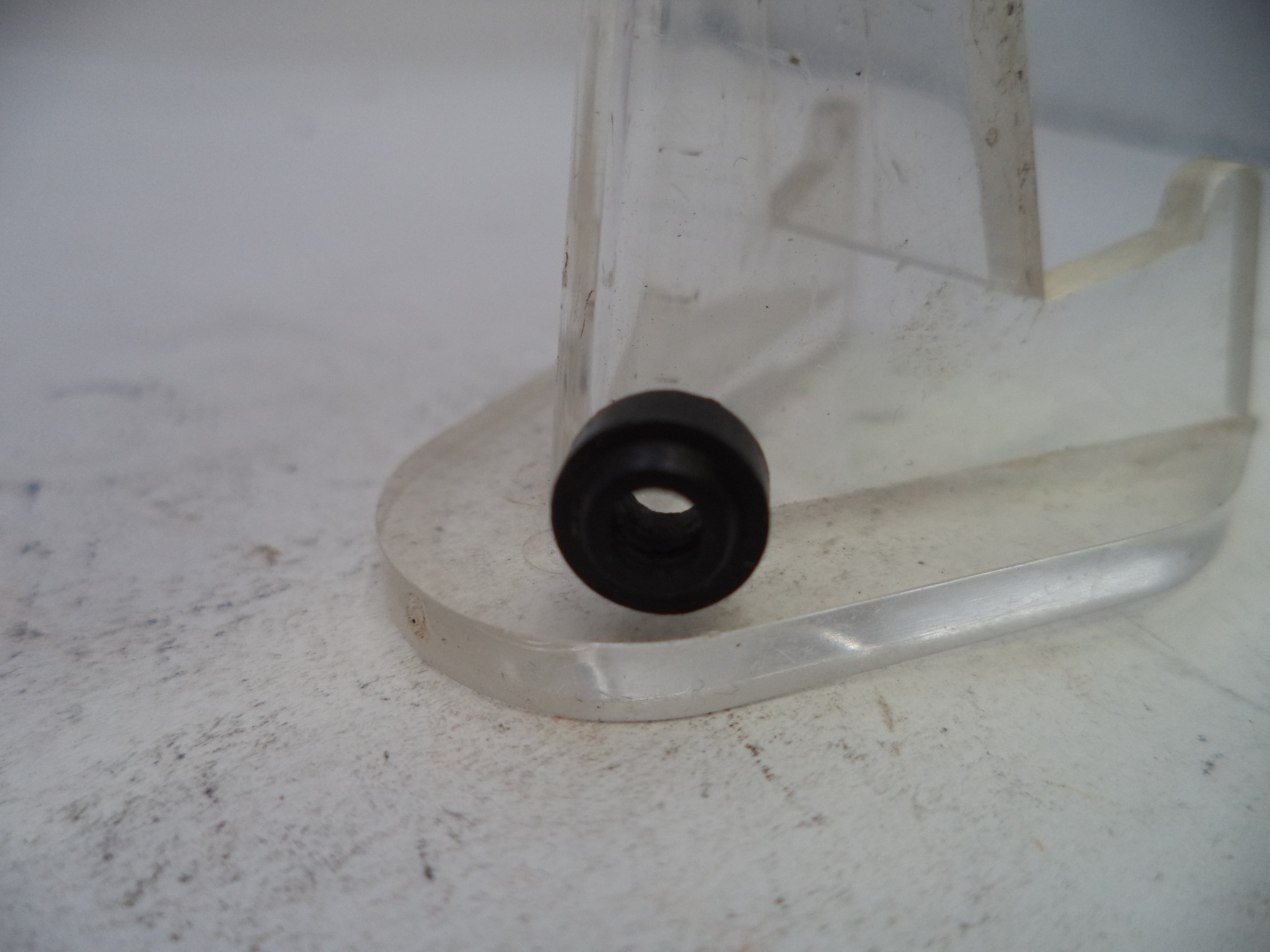 Clear plastic stand with a black rubber bushing on a white surface
