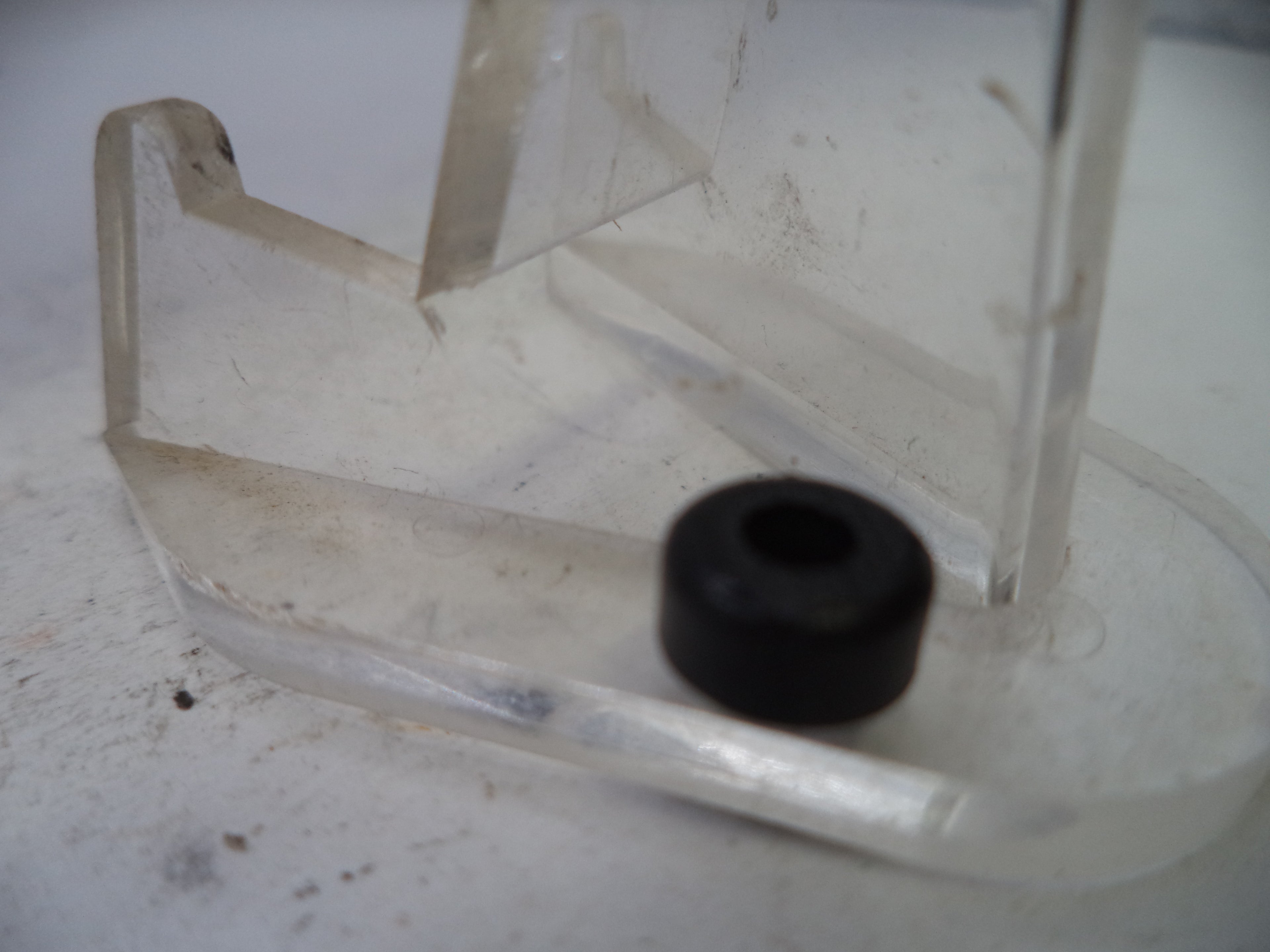Clear plastic component with a black rubber bushing on a white background
