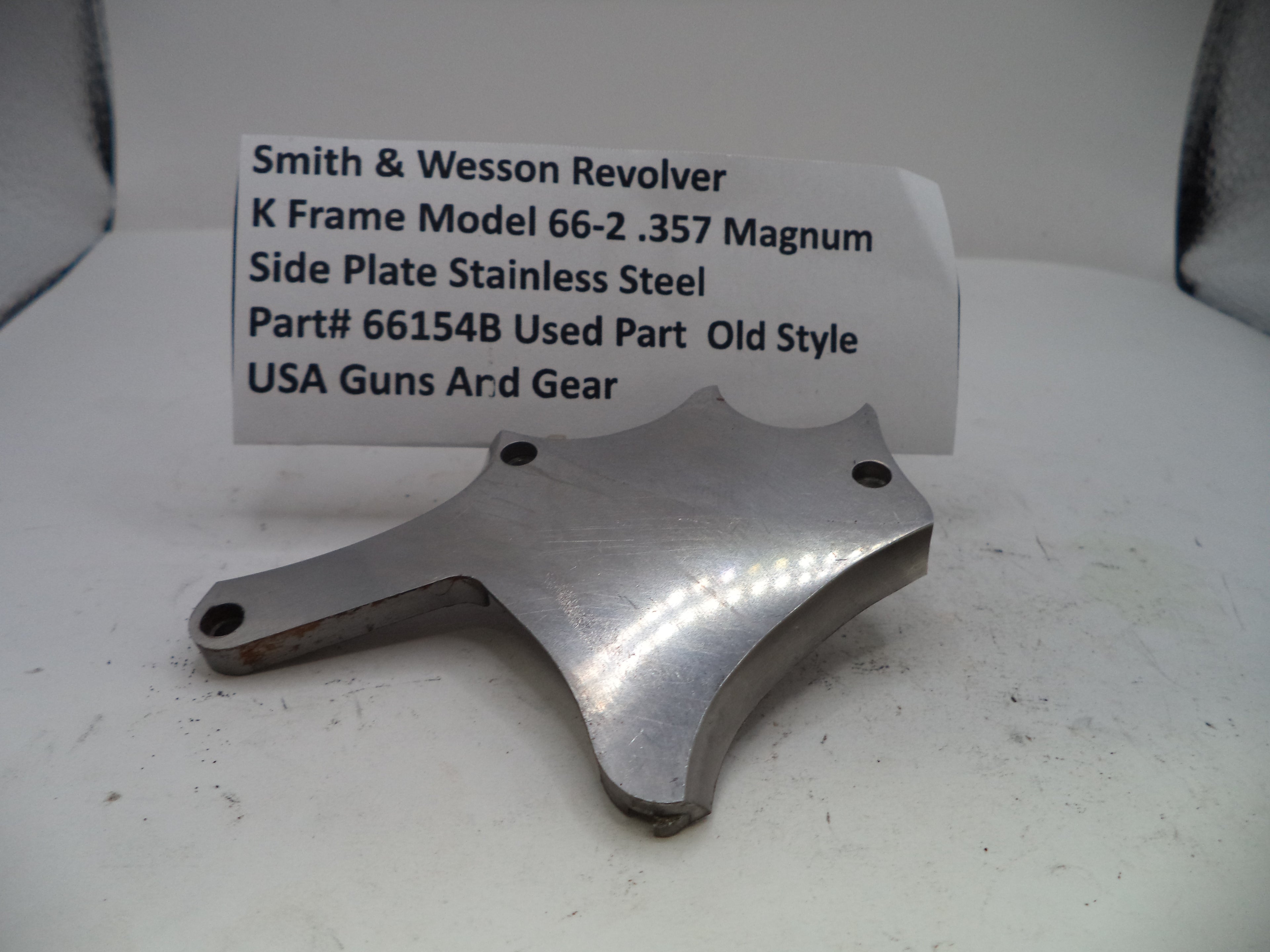 Metal side plate for a Smith & Wesson revolver with descriptive label on a white background