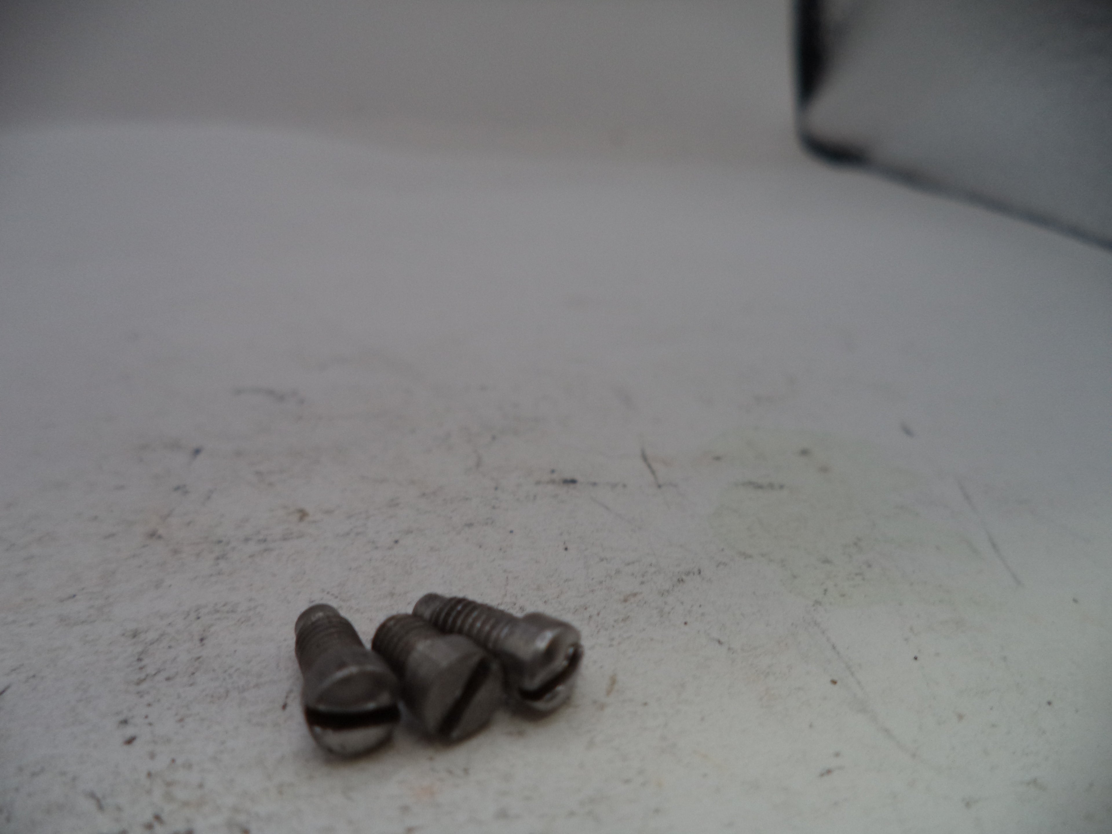 Three metal screws on a white surface with a blurred background
