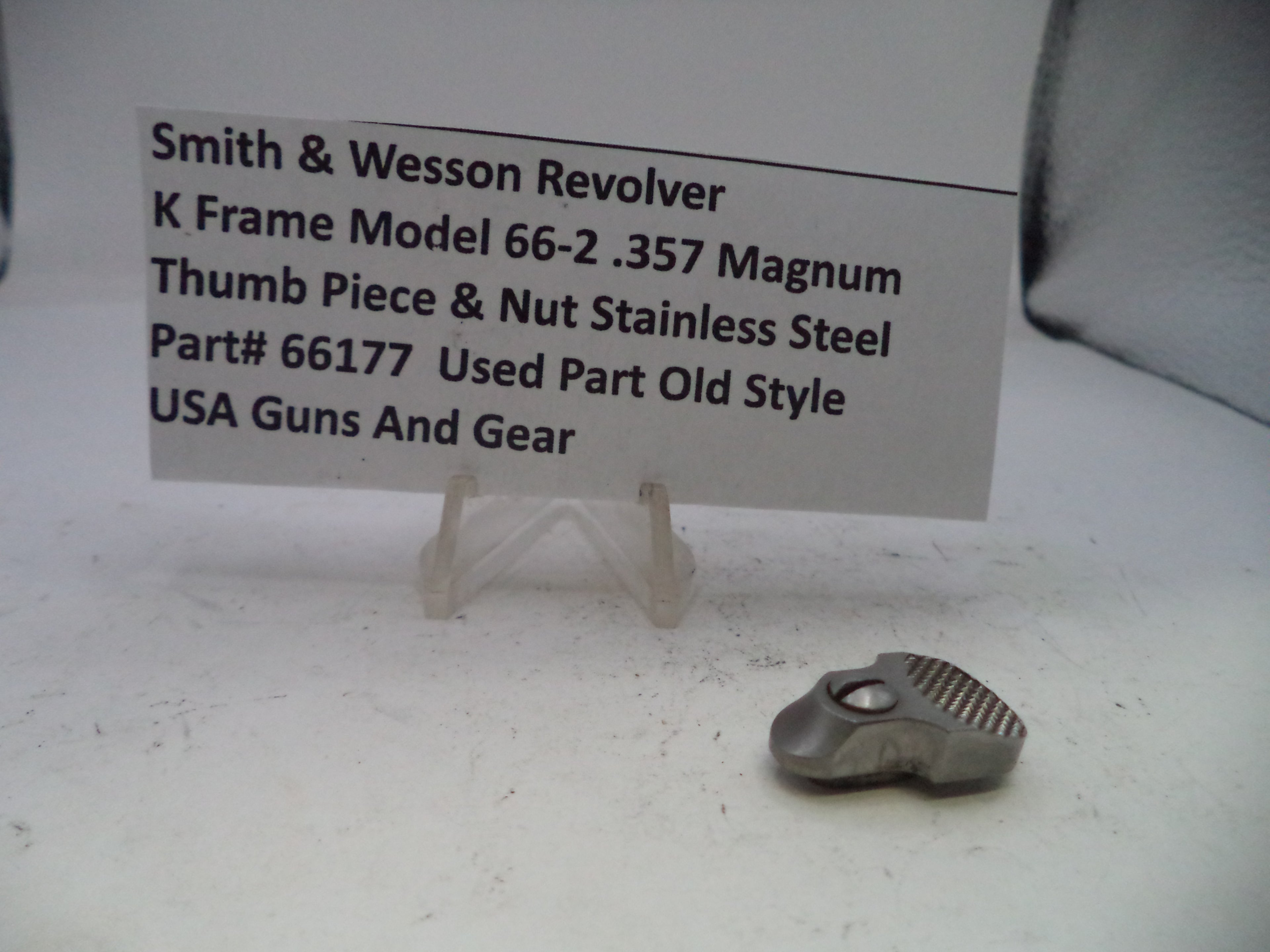 Small metal thumb piece and nut on a white surface with descriptive text card.