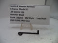 A small black metal hammer block part displayed on a clear stand in front of a white label card that reads 'Smith & Wesson Revolver K Frame Model 12 .38 Special ctg.