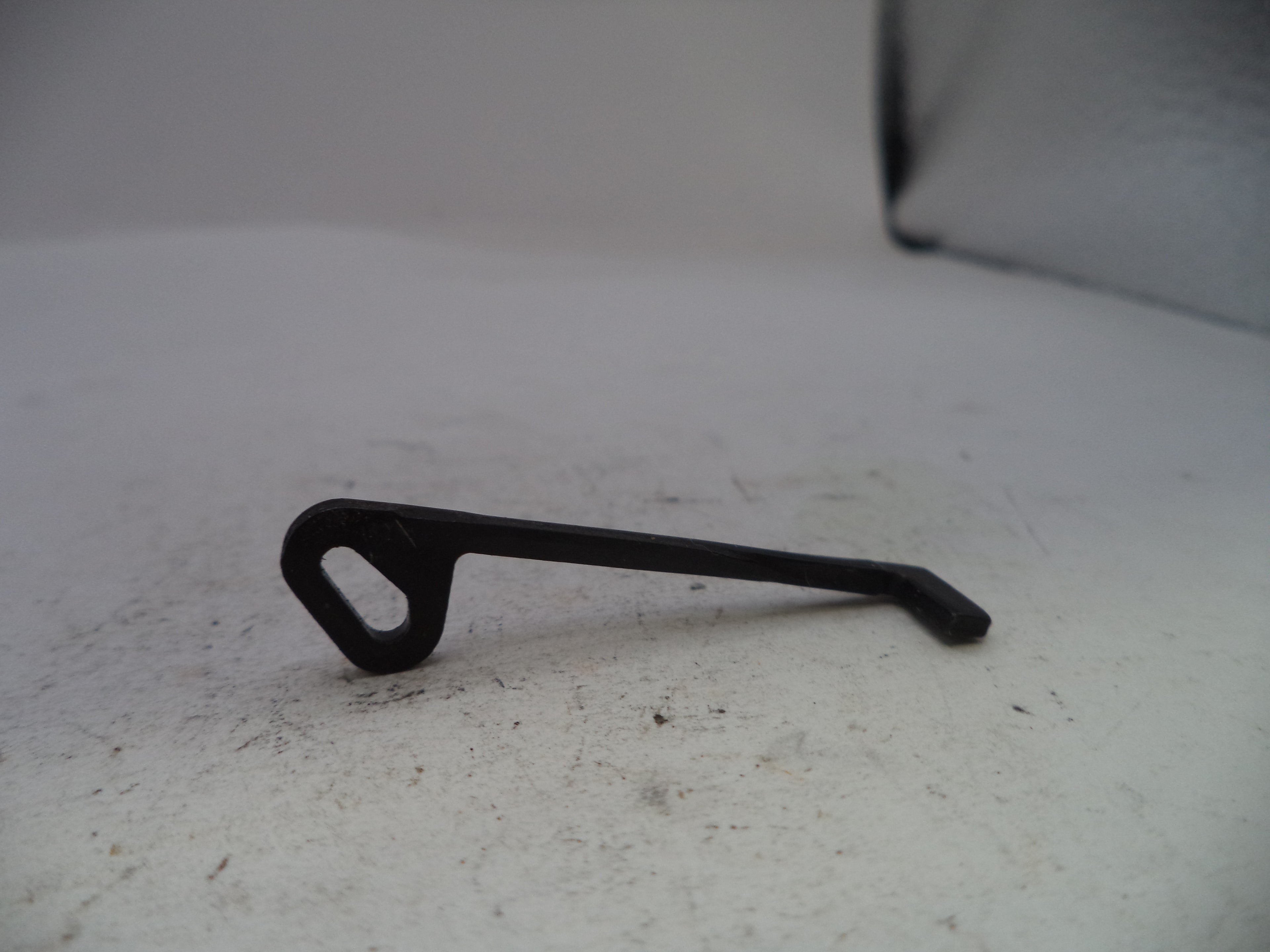 A small black metal latch or hook with a looped end, photographed on a light gray surface.