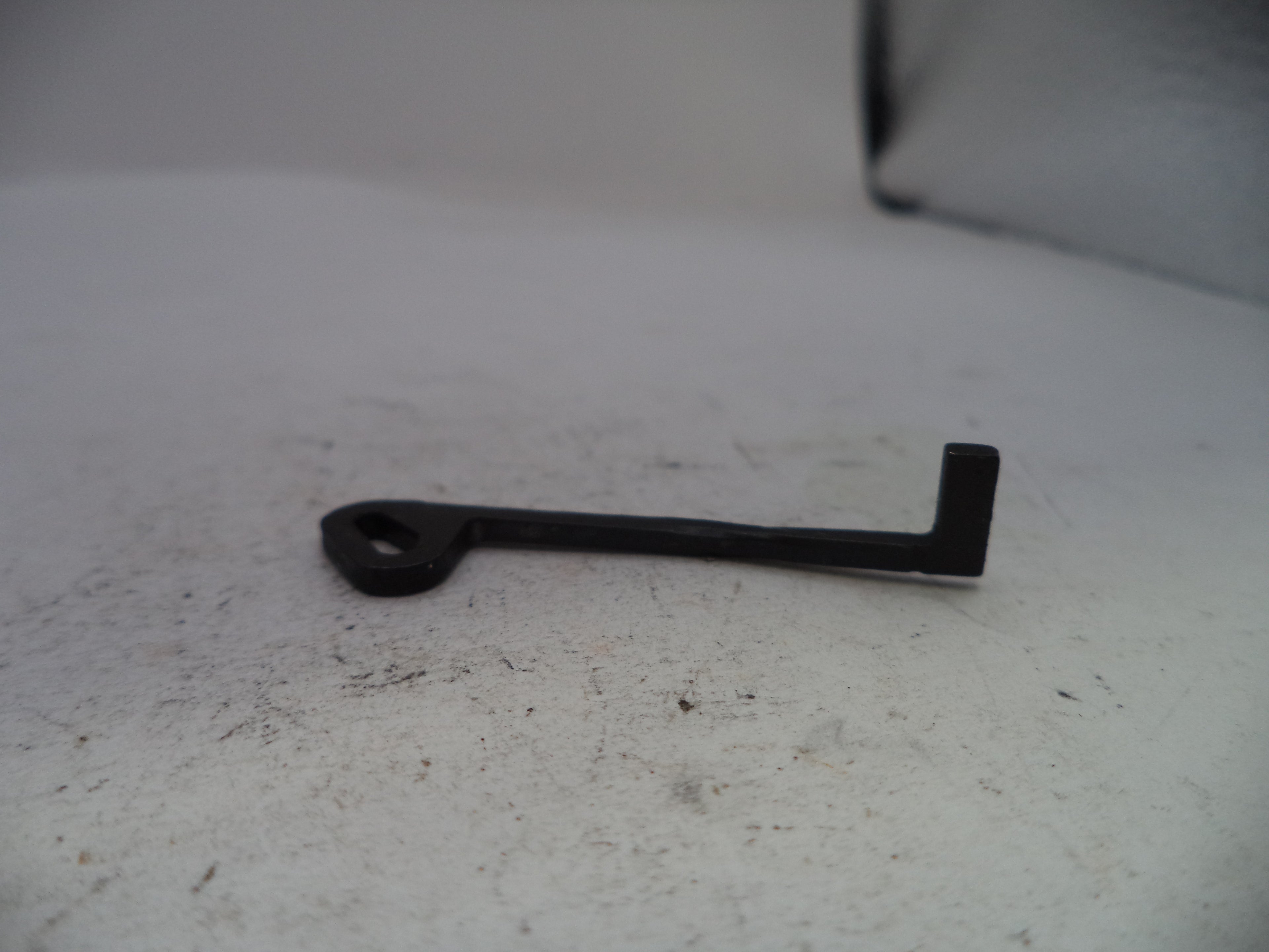 A small black metal key-shaped tool with a looped end, resting on a light gray textured surface.