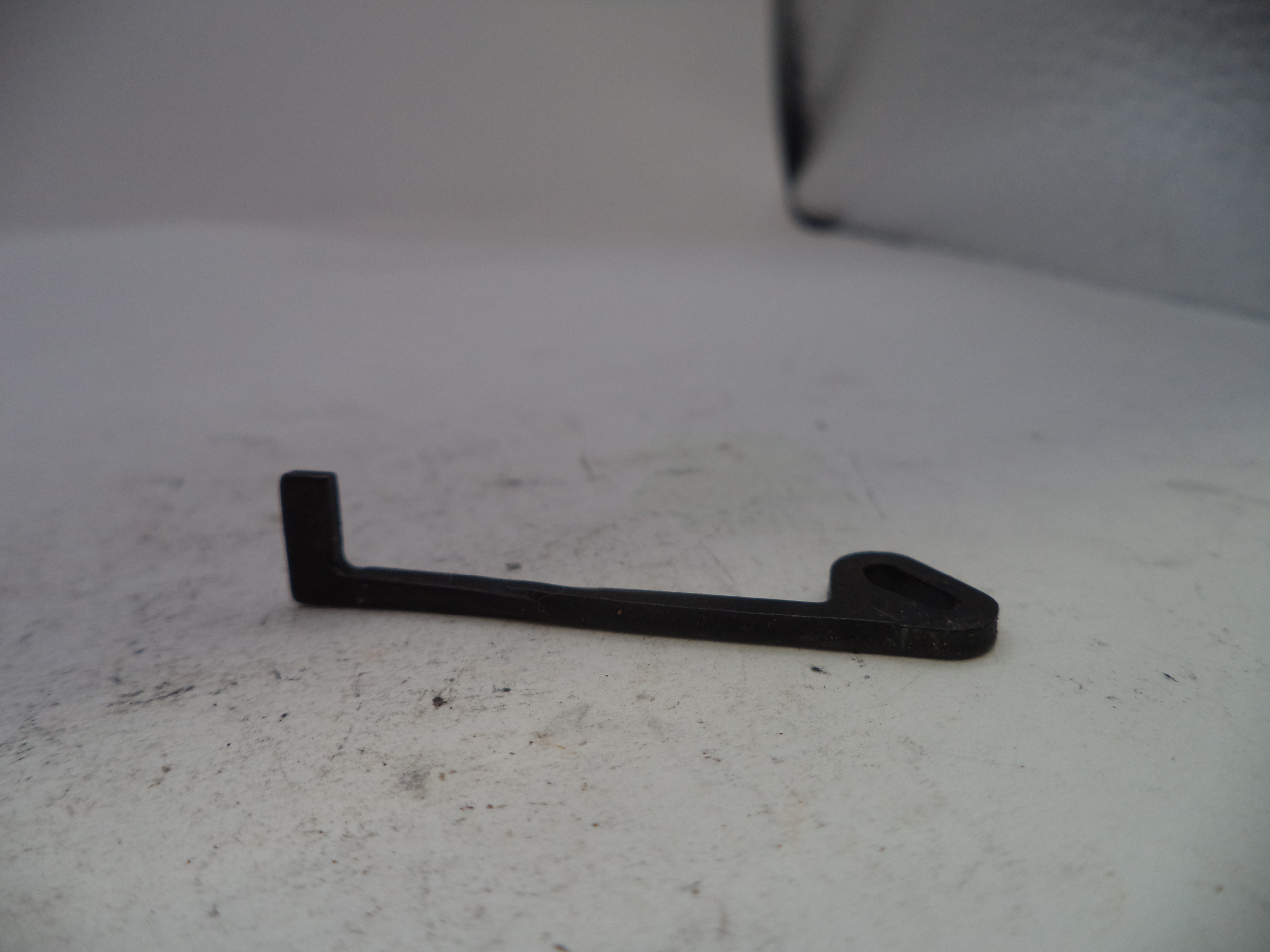 A small black plastic or metal L-shaped bracket with a looped end, resting on a light gray textured surface.