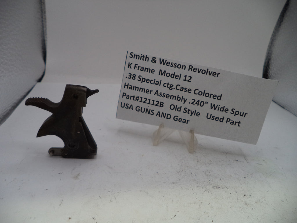 A used metal hammer assembly for a Smith & Wesson revolver, displayed next to a white paper label card on a white surface.