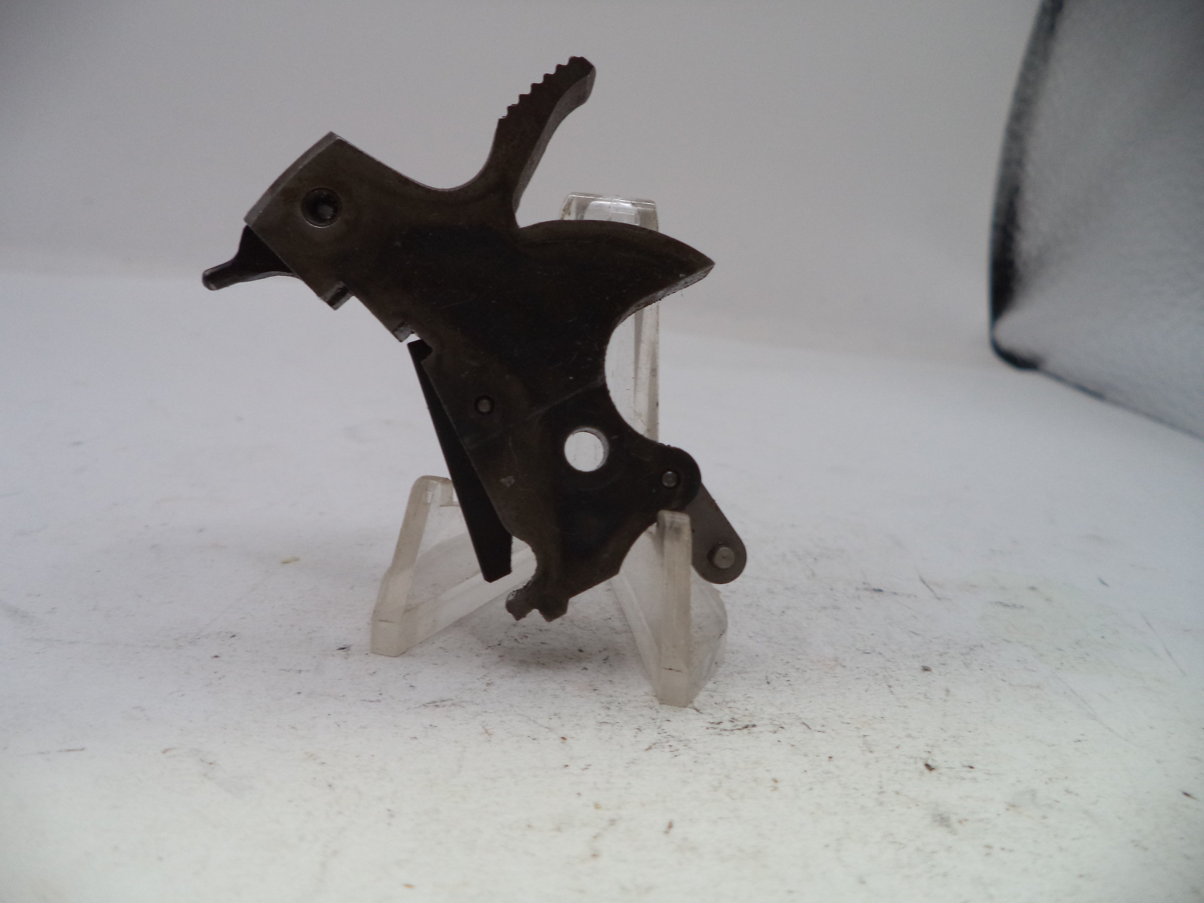 A small dark metal mechanical part or tool component displayed on a clear plastic stand against a plain light background.