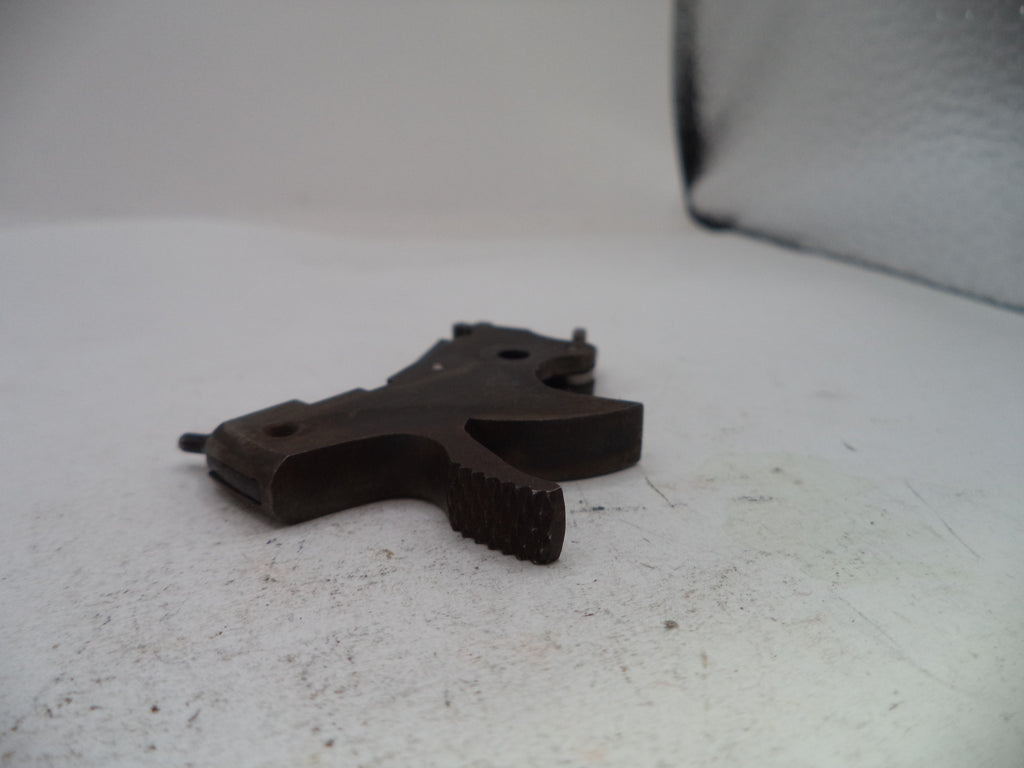 A dark metal firearm trigger assembly, likely a receiver trigger or pistol trigger component, resting on a white surface.