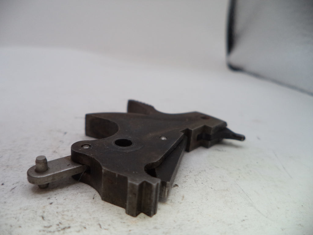 A dark metal mechanical component or tool part with a worn, used surface, photographed on a white surface with a soft-focus background.
