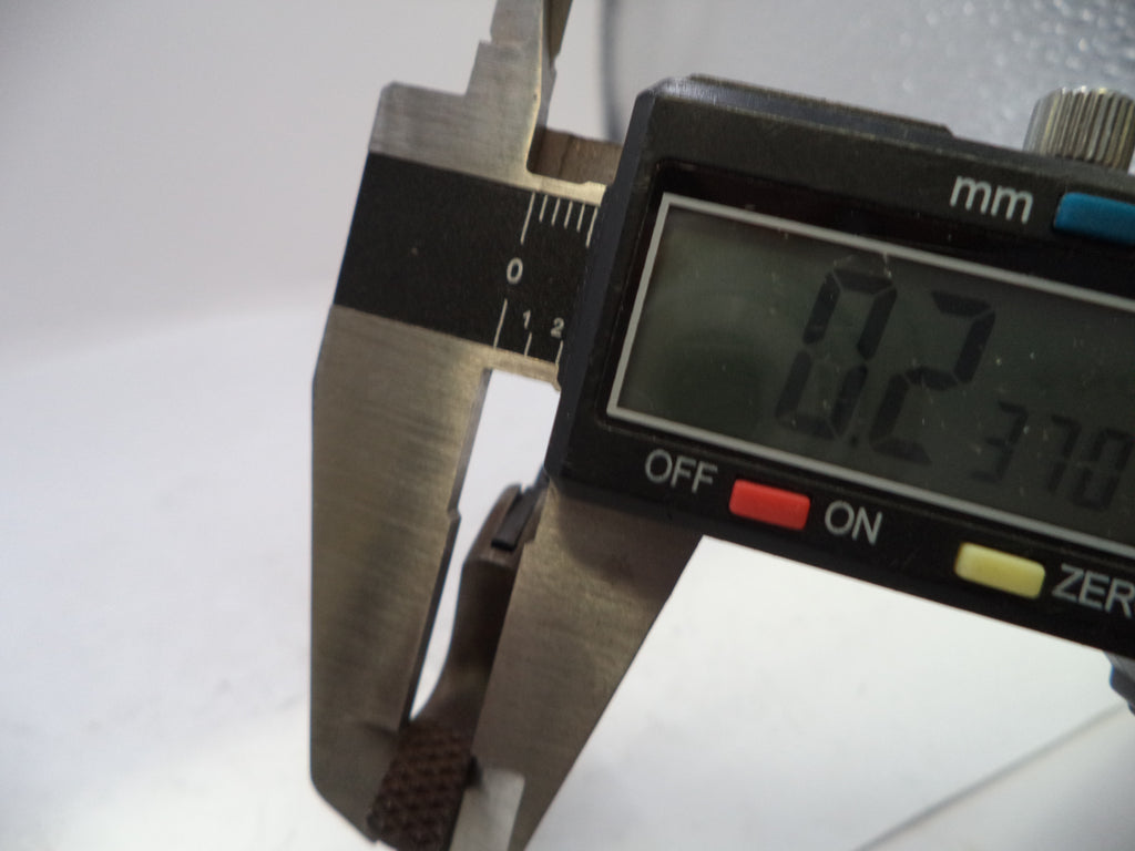 Close-up of a digital caliper measuring a small brown textured strap, with the display reading 0.23 mm.