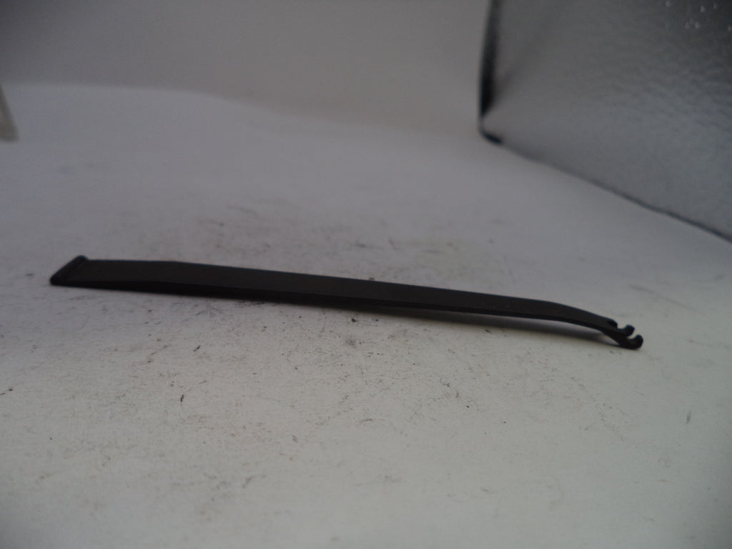 A long, thin black plastic or rubber tool with a hooked end, lying on a light gray textured surface.