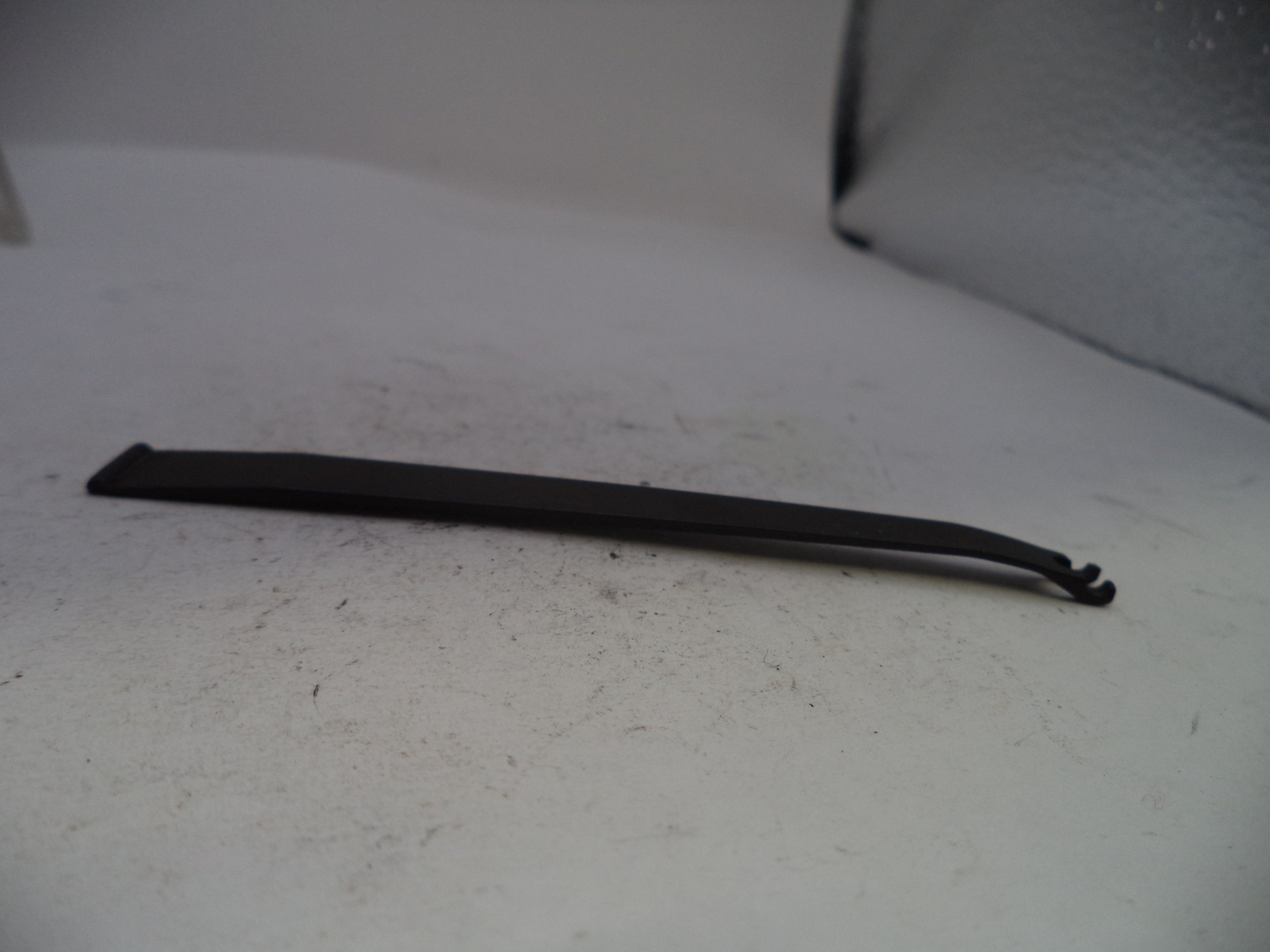 A long, thin black plastic or rubber tool with a hooked end, lying on a light gray textured surface.