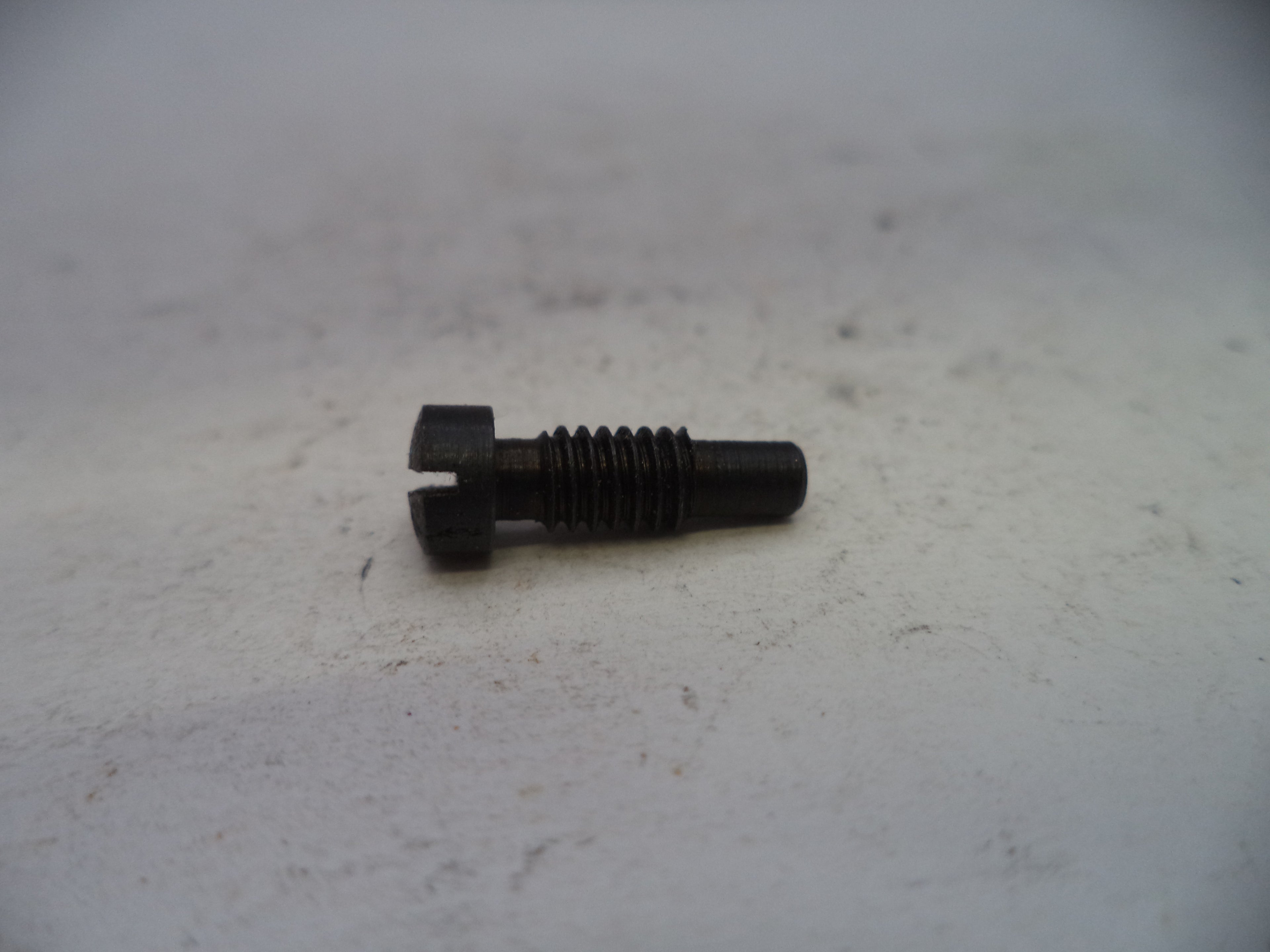 A small black metal threaded bolt or screw with a slotted head, resting on a light gray textured surface.