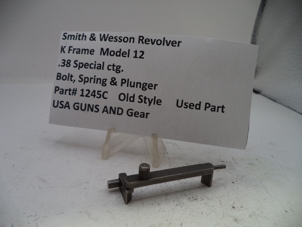 A used metal part for a Smith & Wesson Revolver K Frame Model 12, shown on a clear stand with an informational paper label.