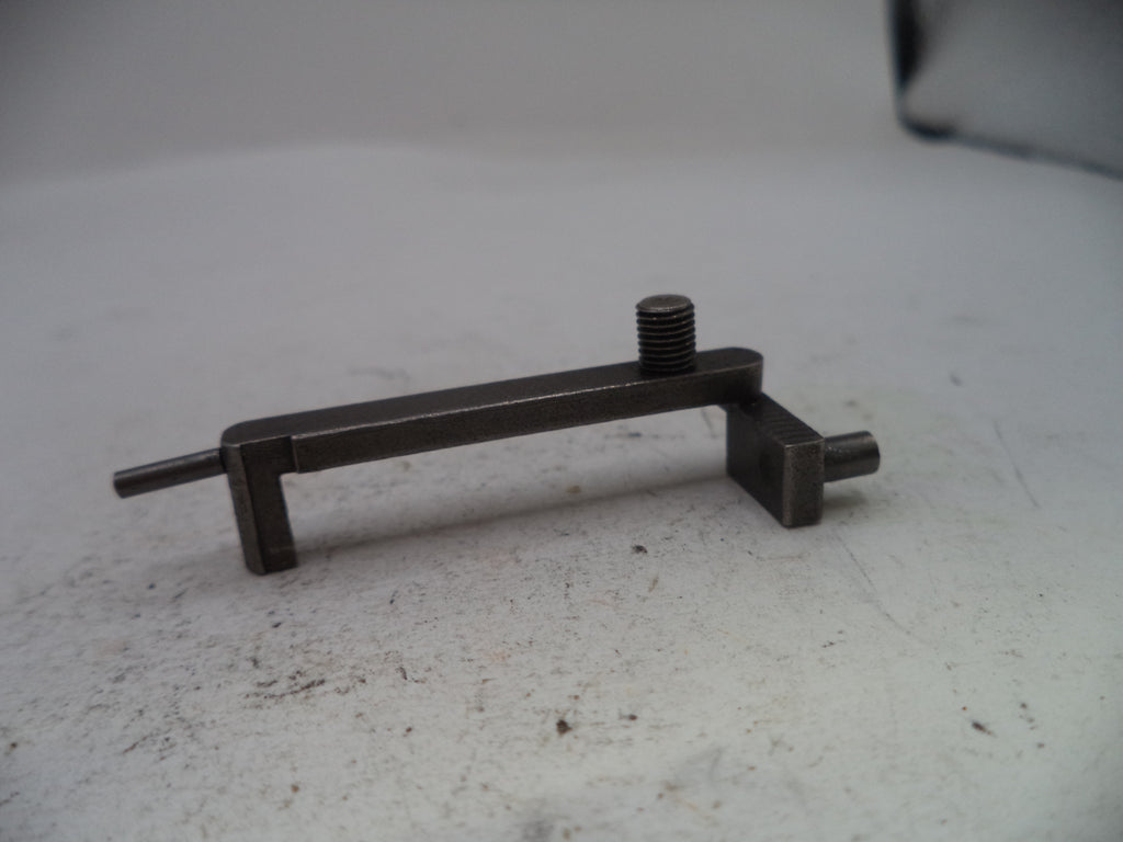 A small dark metal mechanical component with a threaded screw and flat shafts, resting on a light gray surface.