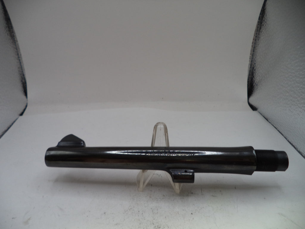 A black metal cylindrical component, likely a firearm barrel or tube, displayed horizontally on a clear plastic stand against a white backdrop with textured black corners.
