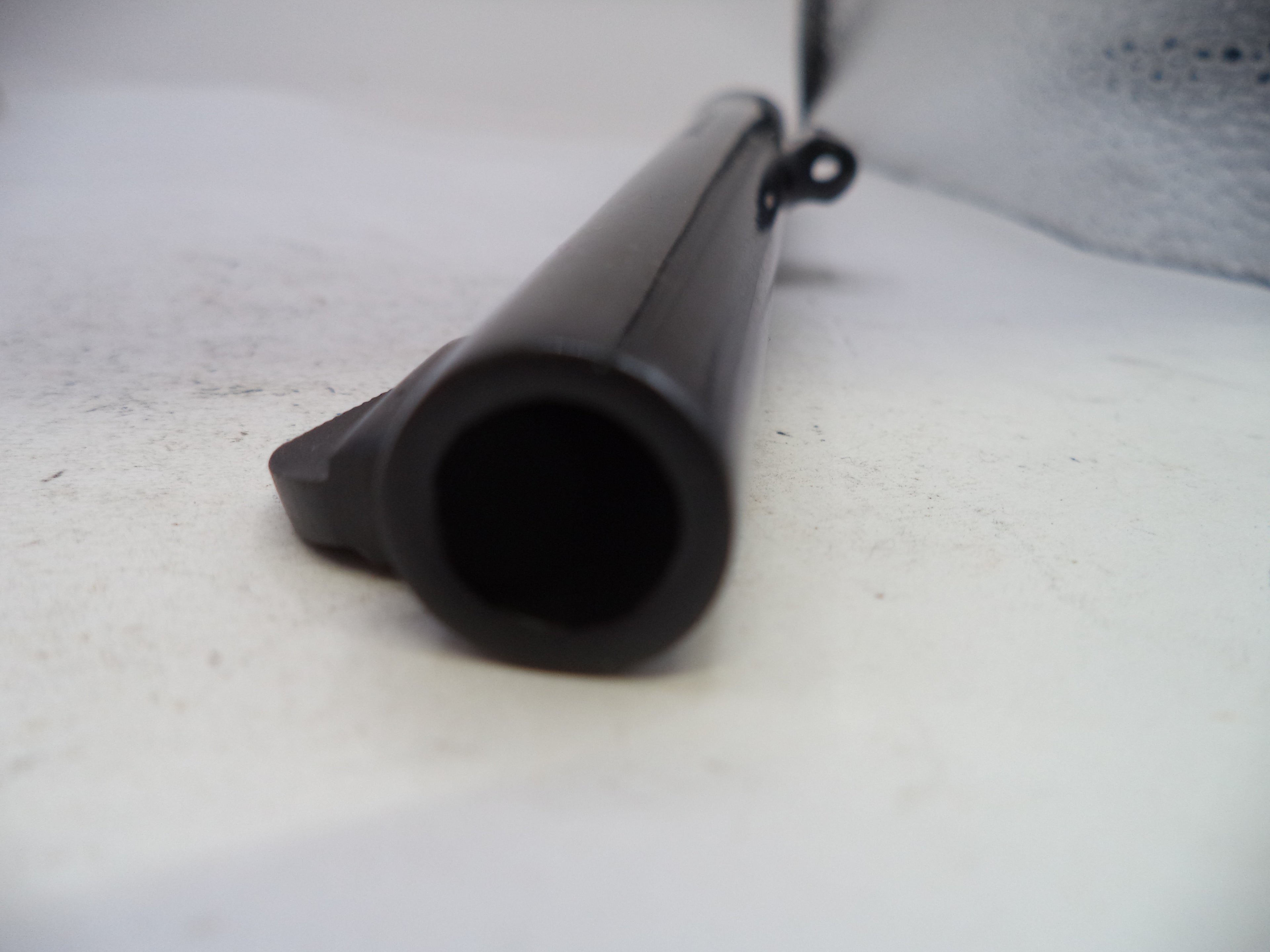 A close-up shot of a black cylindrical product, possibly a barrel or tube, lying on a light-colored, slightly textured surface.