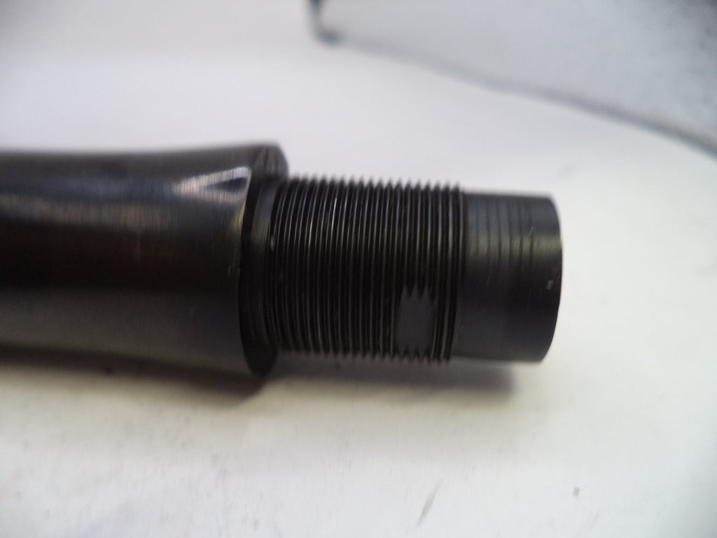 A close-up of a black metal threaded component, possibly a mechanical fitting or valve stem, resting on a white surface.