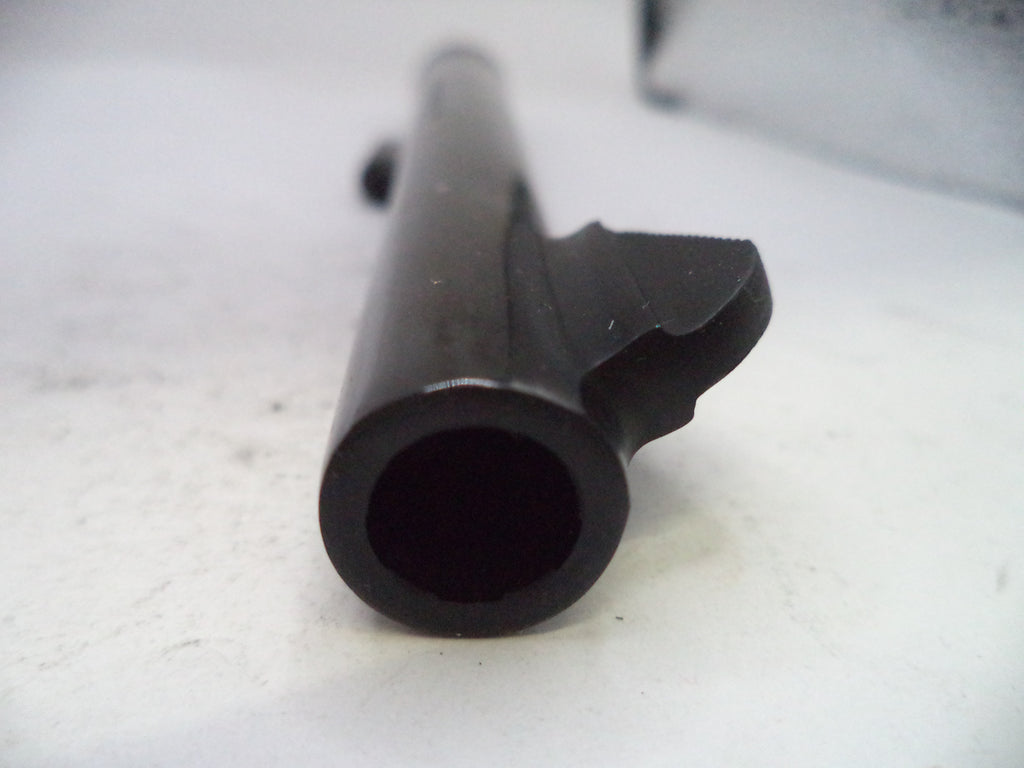 A close-up shot of a black metal cylindrical component, possibly a barrel or tube, with a bracket or clip attached on one side, resting on a light-colored surface.
