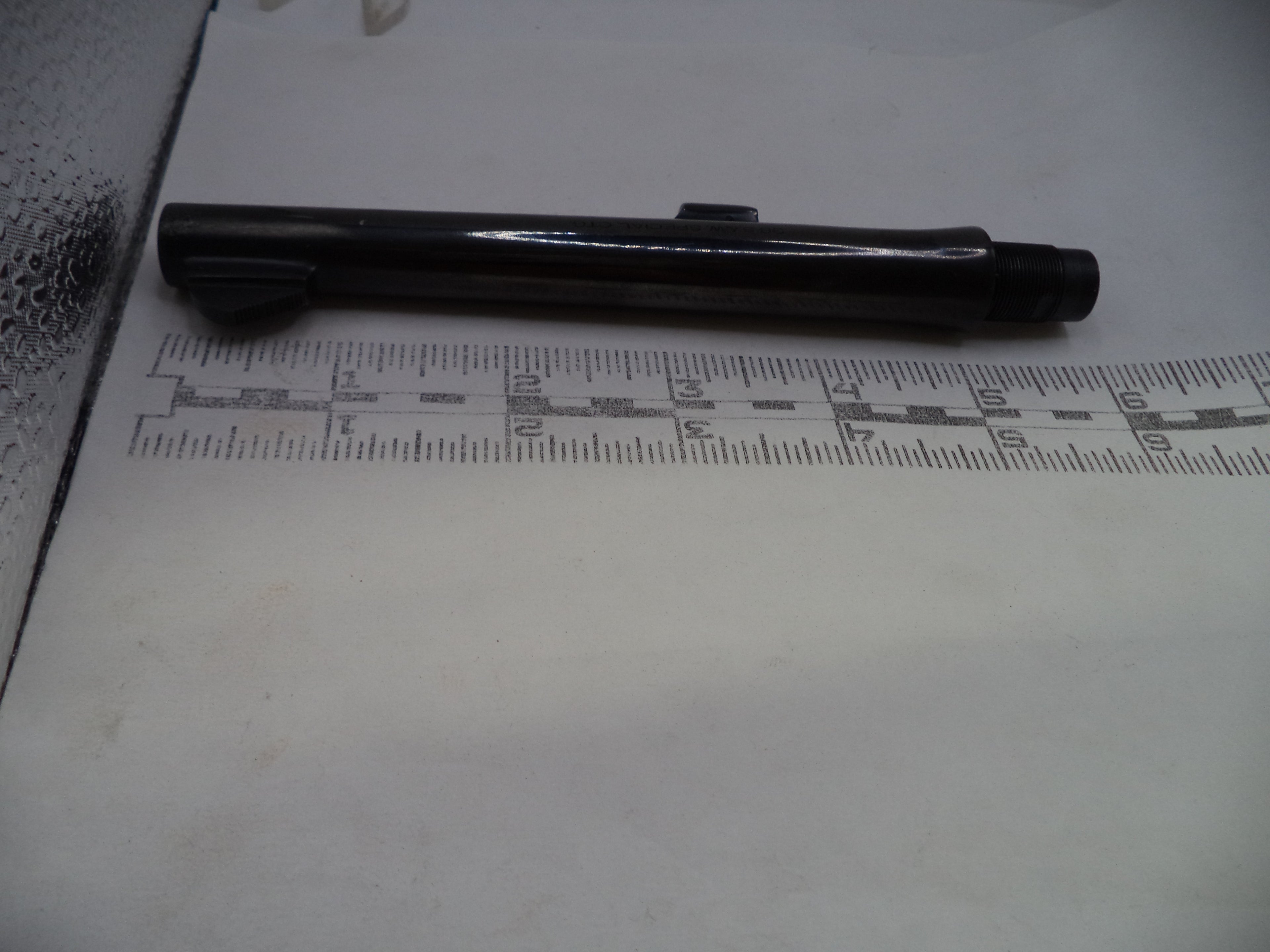 A black cylindrical pen-like object placed horizontally on a white surface, with a ruler underneath for scale.