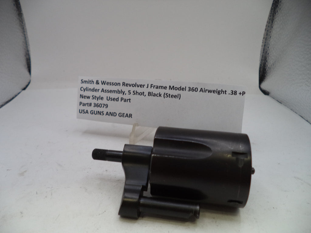 A black Smith & Wesson revolver cylinder assembly part, photographed on a white surface with a handwritten label card behind it.