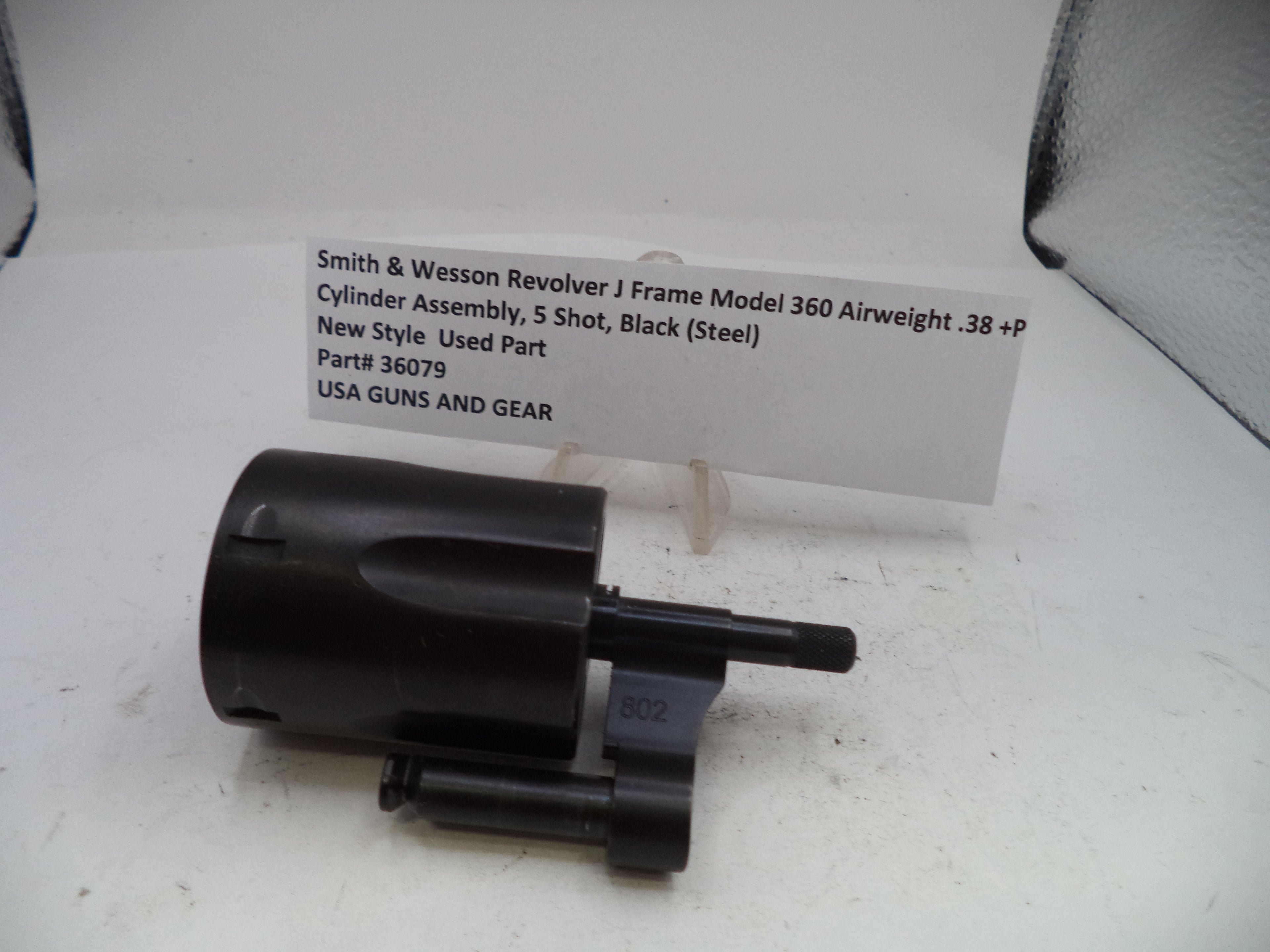 A black Smith & Wesson Revolver J Frame Model 360 airweight cylinder assembly, used part, displayed on a white surface with a paper label card behind it.