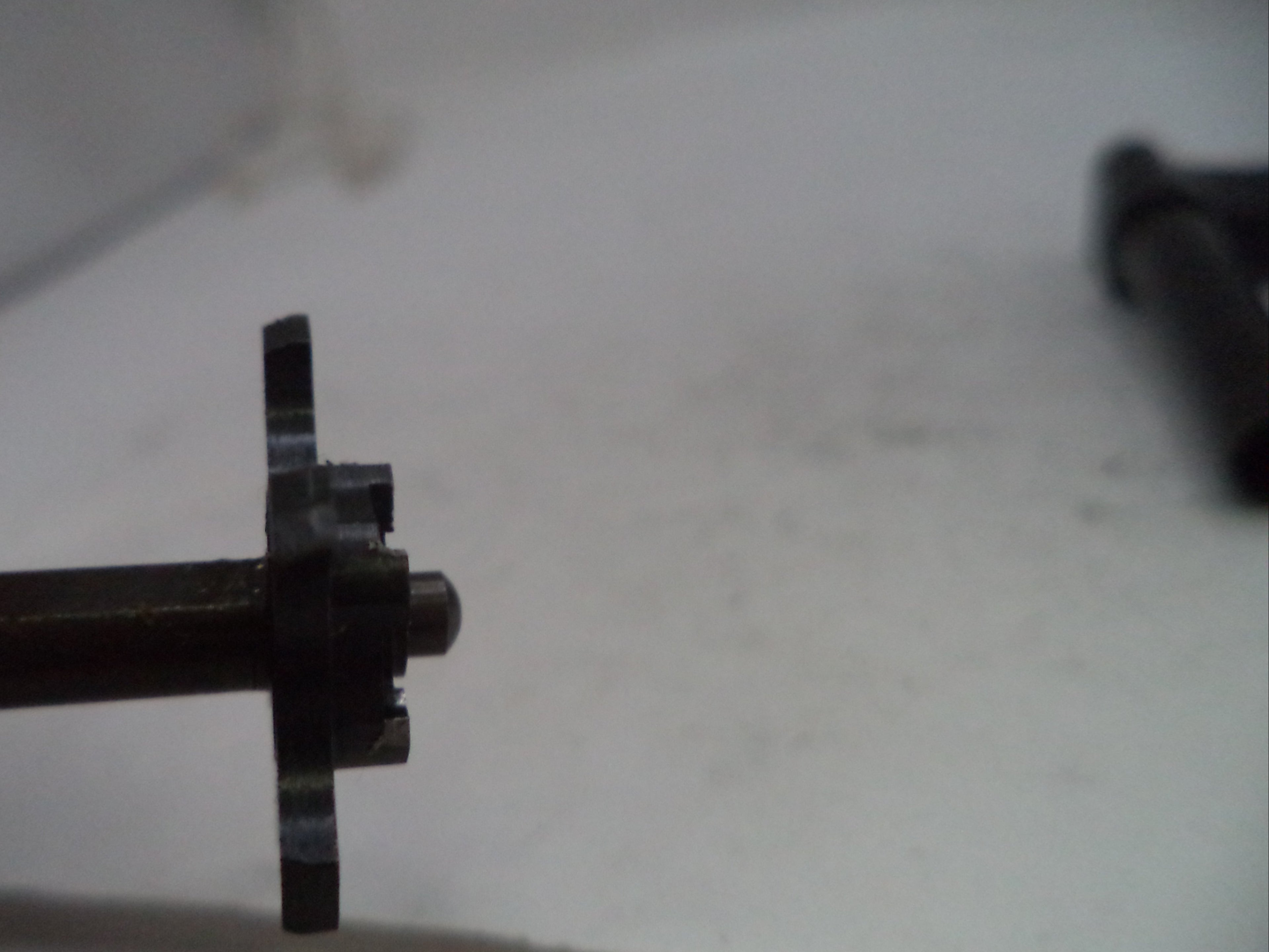 A close-up of a small black metal mechanical component held by fingers against a light gray background.