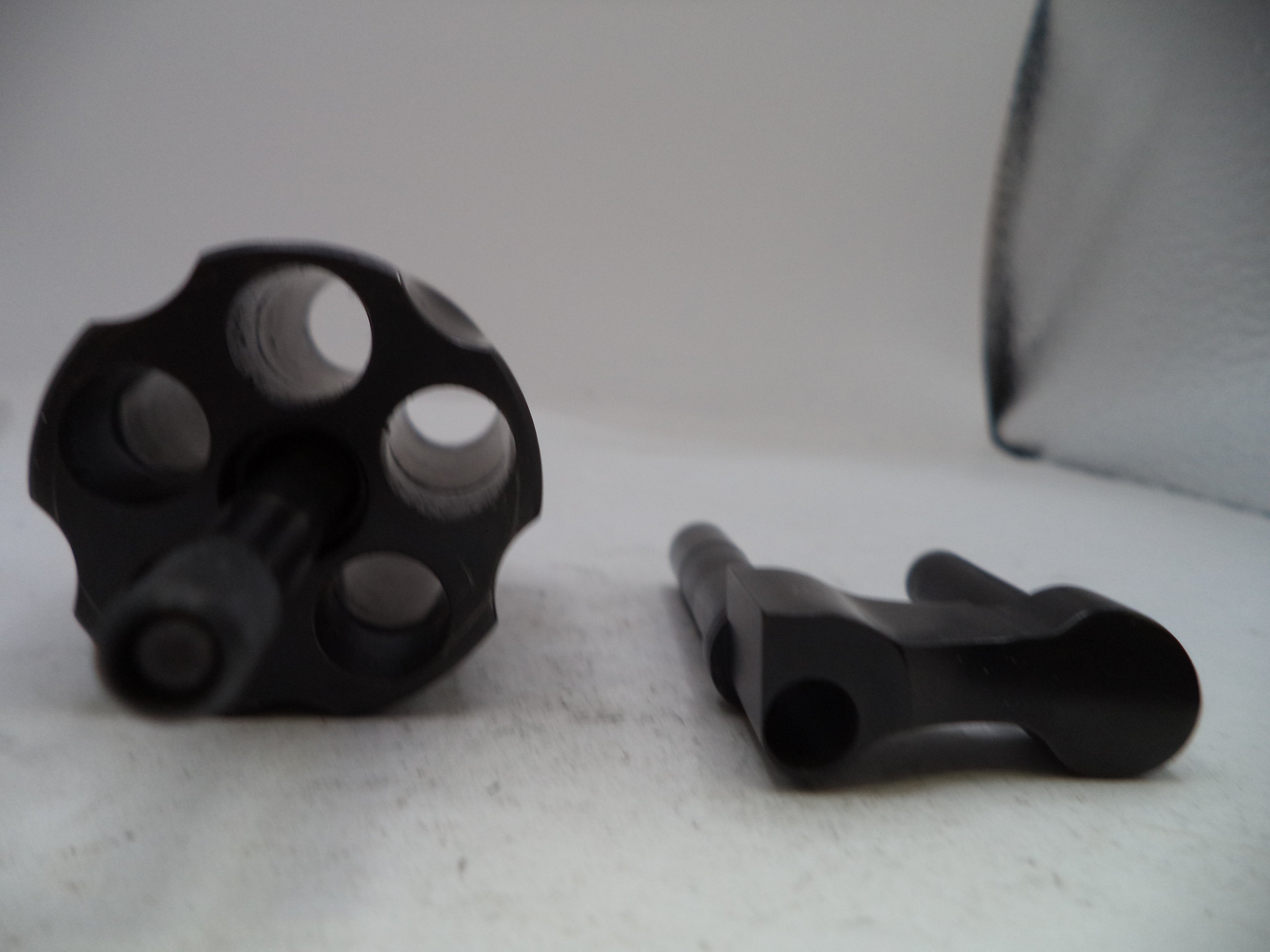 A black metal revolver-style accessory with a six-hole cylinder and a separate black mounting piece, photographed on a light gray surface.