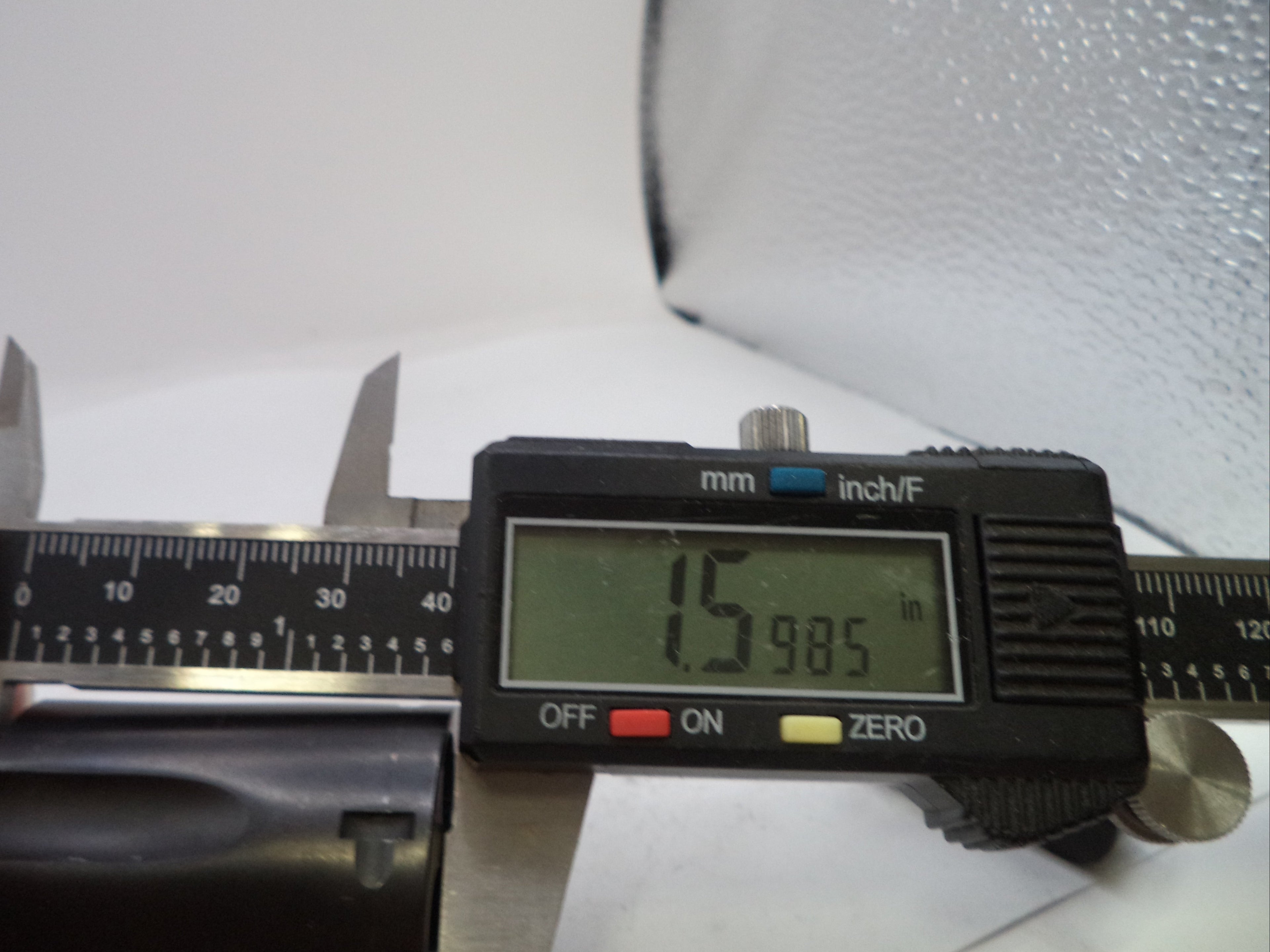 A close-up of a digital caliper being used to measure a cylindrical item, with a hand holding the left side. The caliper display shows 15.