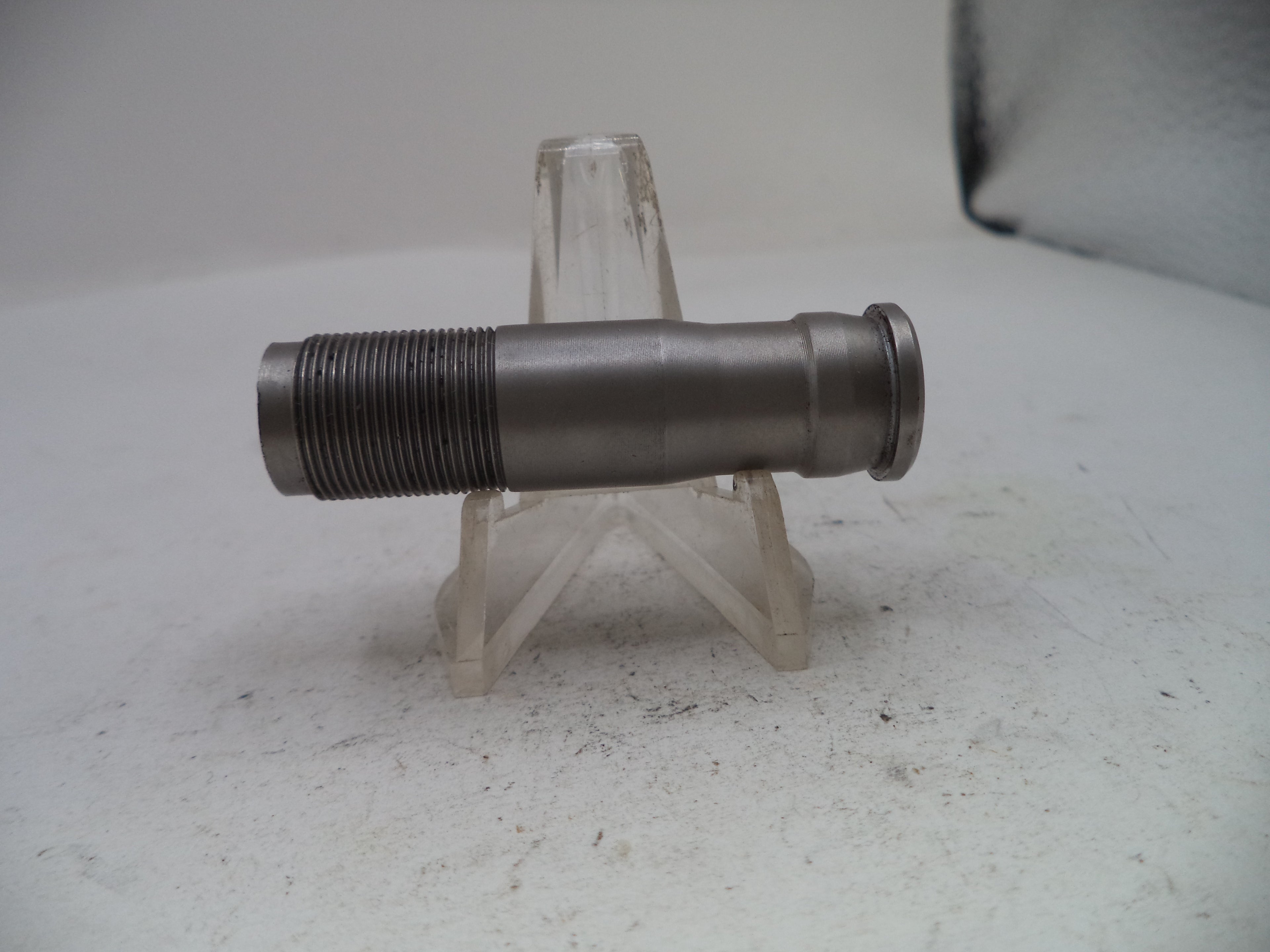 A metallic cylindrical threaded component, likely a mechanical part or fitting, displayed horizontally on a clear plastic stand against a light gray background.
