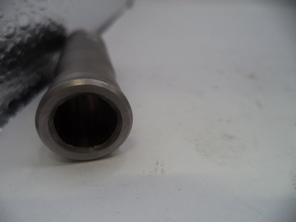 A close-up shot of a metallic cylindrical component, showing a machined silver-gray end with a dark interior, resting on a light gray surface.