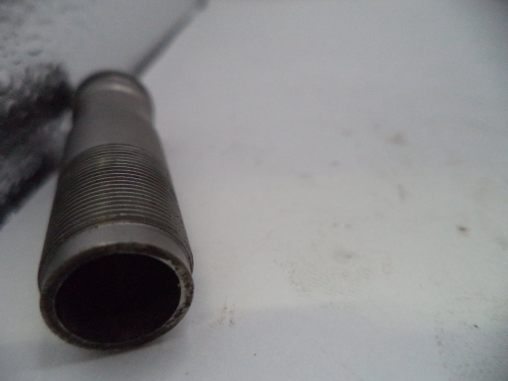 A close-up of a threaded metal rod or pipe fitting on a white surface.