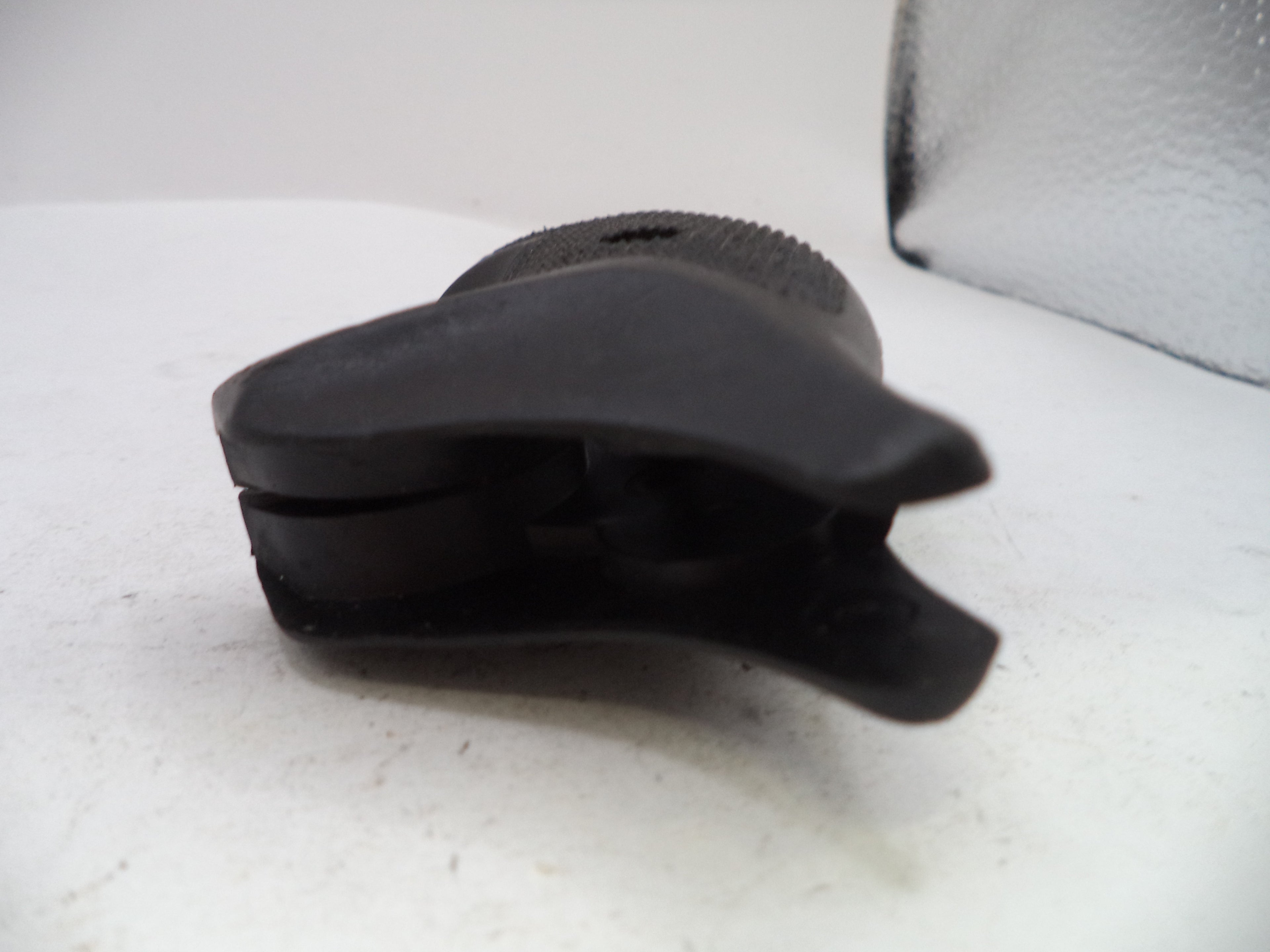 A black plastic replacement part, possibly a clip or bracket, shown on a white surface with a textured gray background.