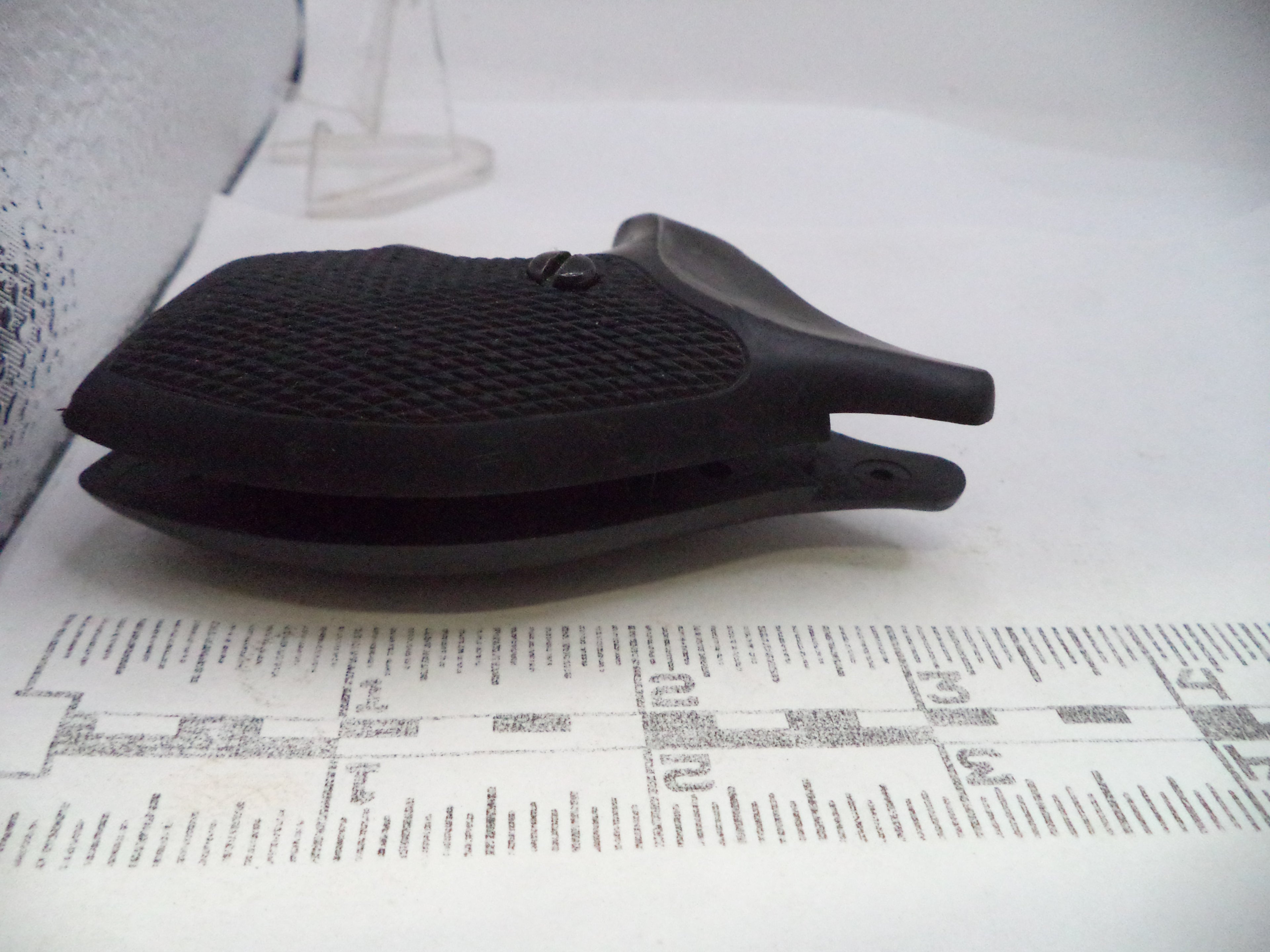 A black textured plastic clip or holder shown on a white surface with a printed ruler in the foreground for scale.