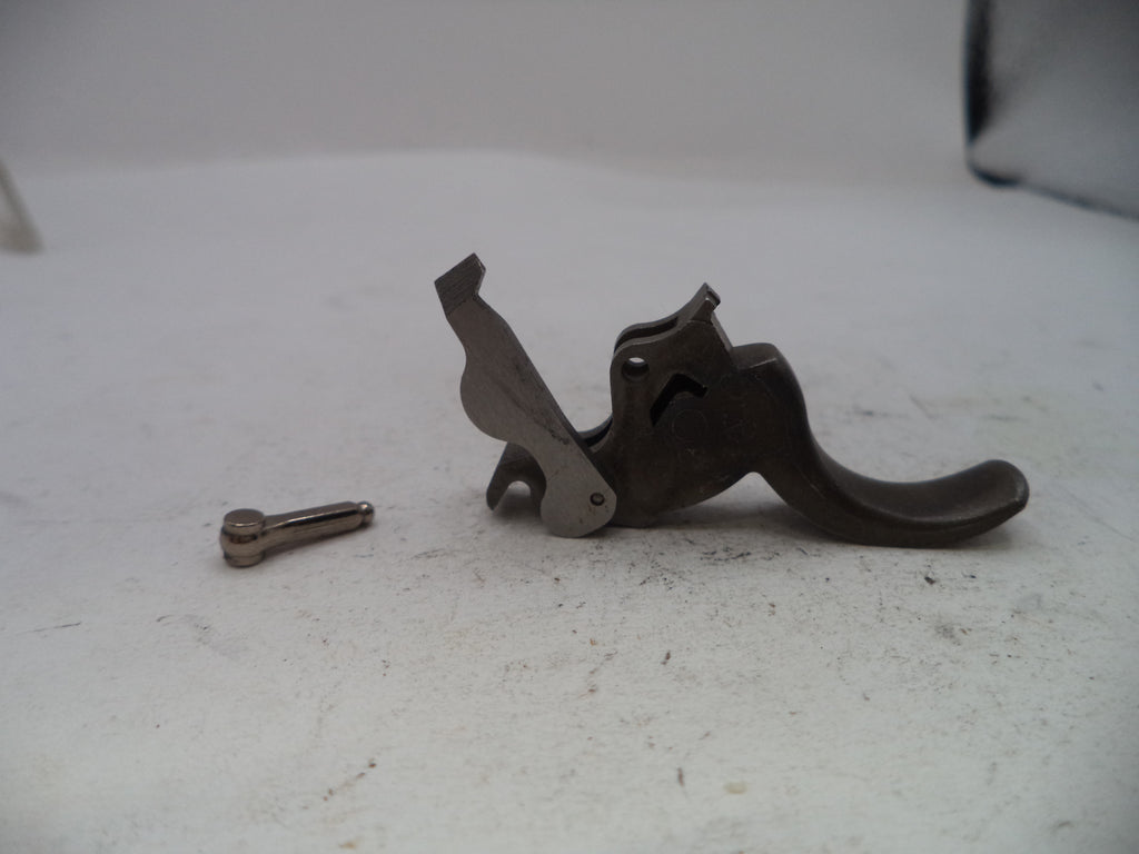 A small dark metal mechanical component with a curved lever and a separate small metal pin or screw placed beside it, photographed on a light gray surface.