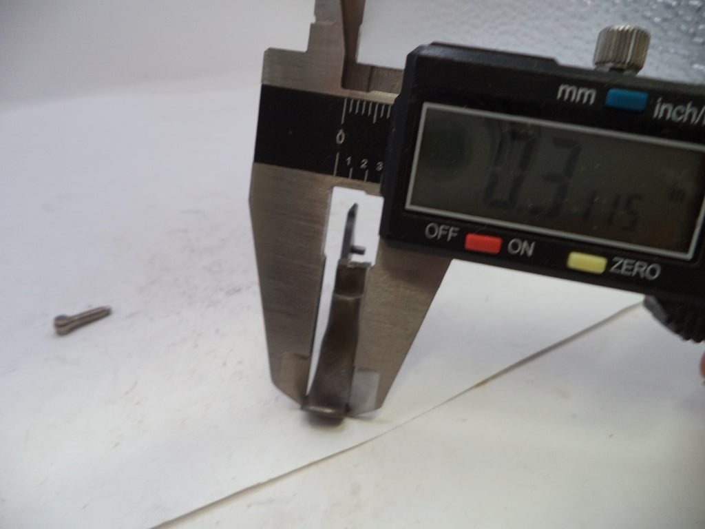A close-up of a digital caliper measuring a small metal component, with a loose matching screw on a white surface nearby.