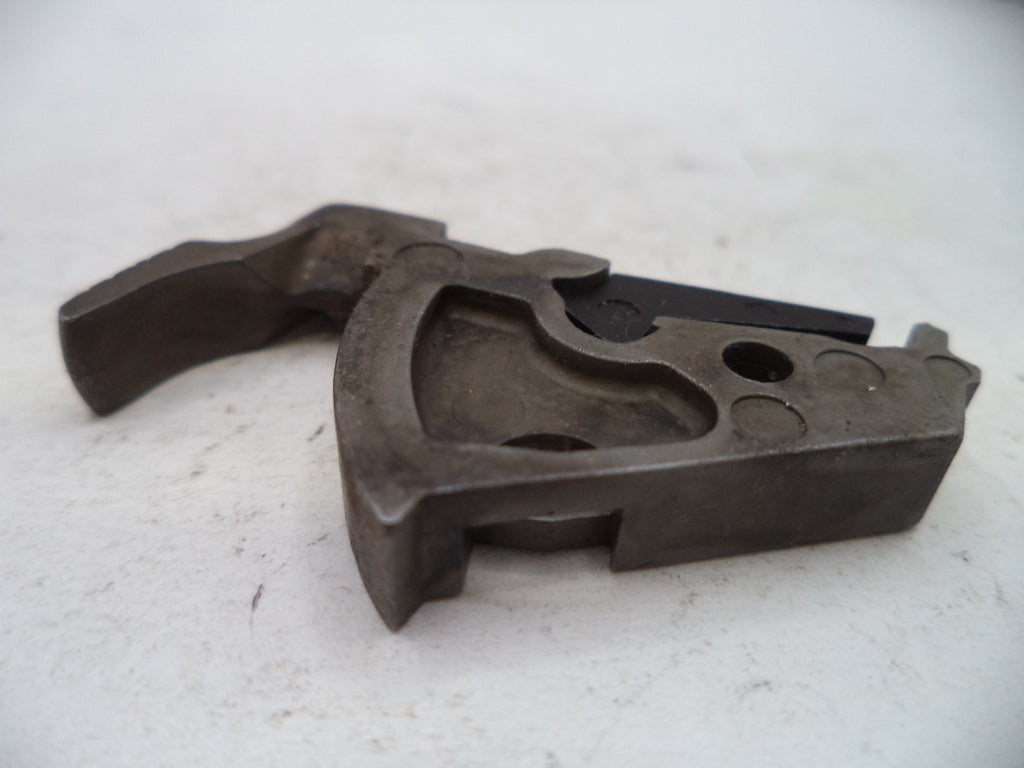 A dark metal mechanical component or tool part with a curved handle and circular cutouts, photographed on a light off-white surface.