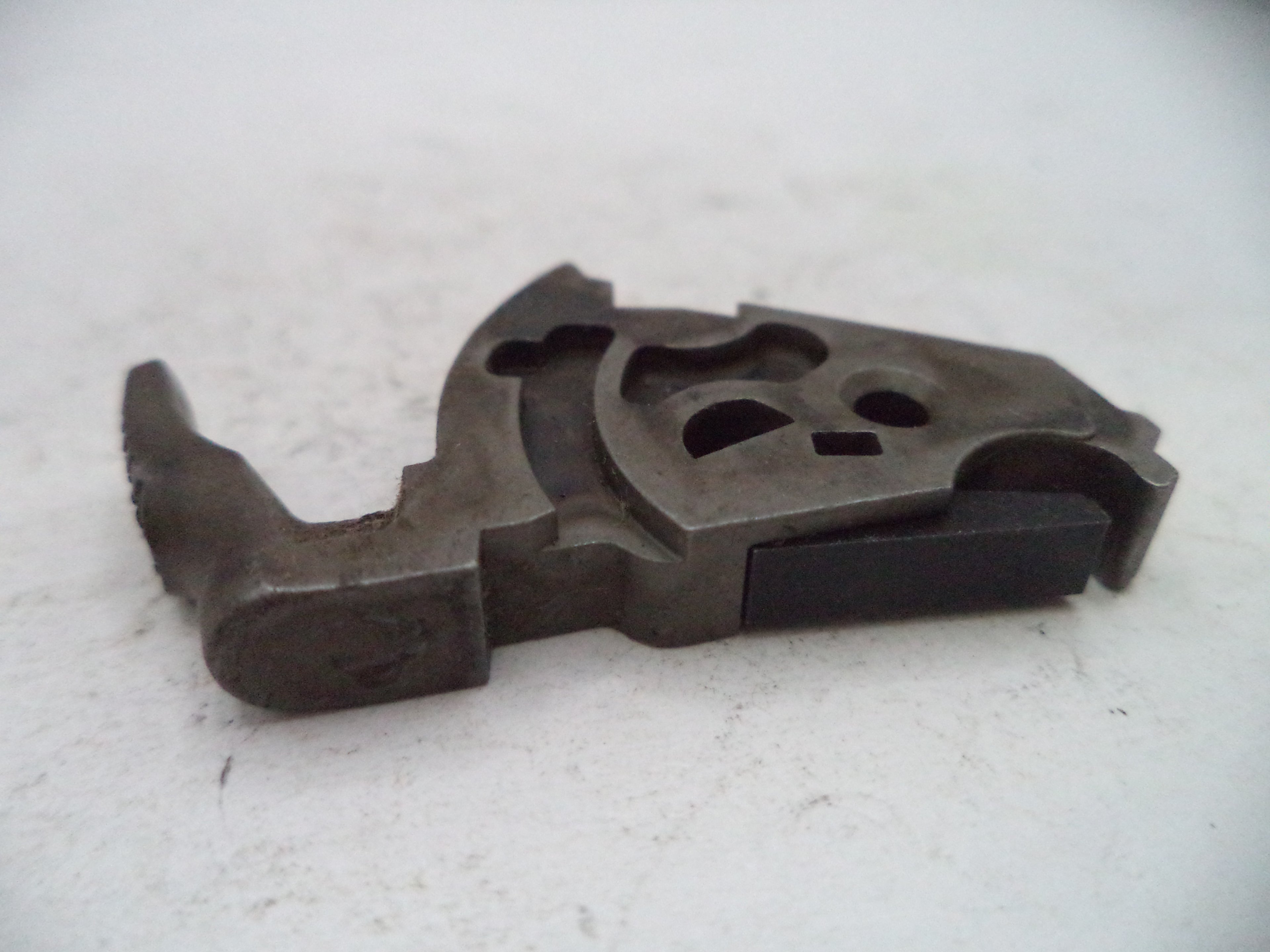 A dark gray metal mechanical component with a skull-shaped cutout, photographed on a white textured surface.