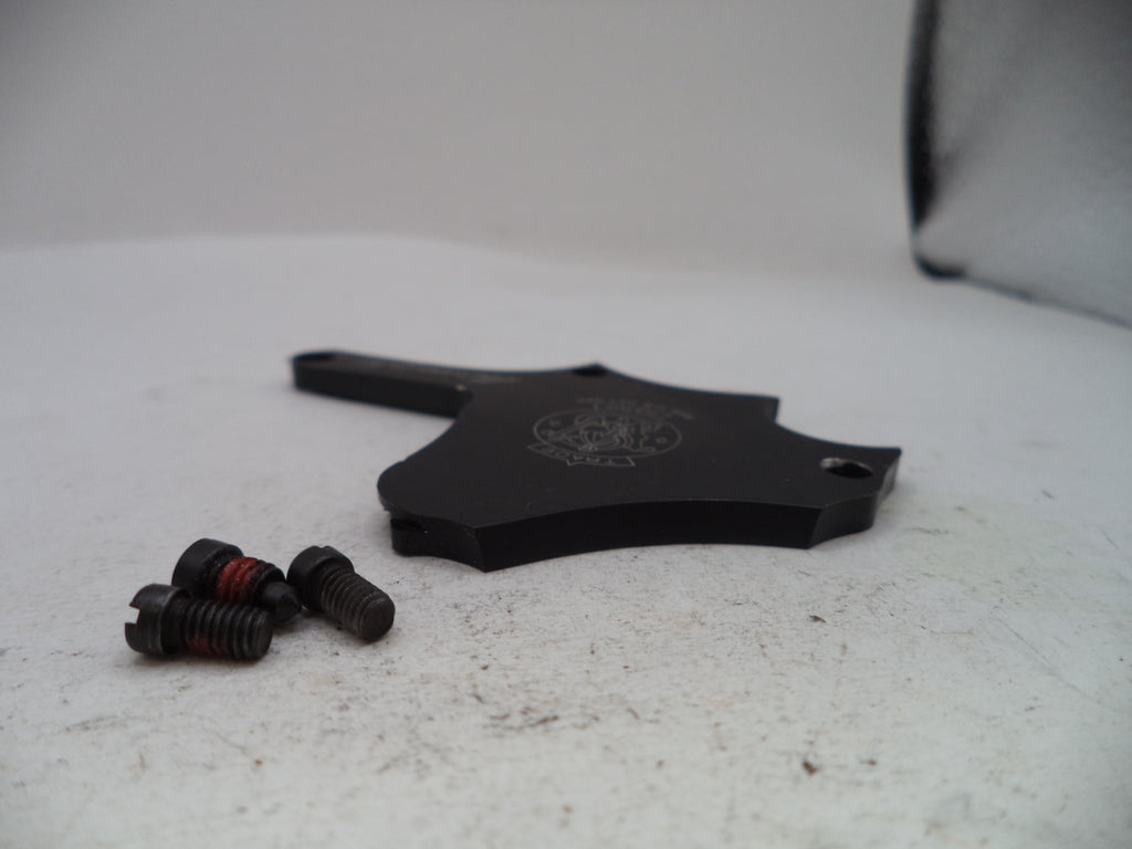 A black metal mounting bracket with a hexagonal profile and three small black screws with red thread wraps, placed on a light gray textured surface.