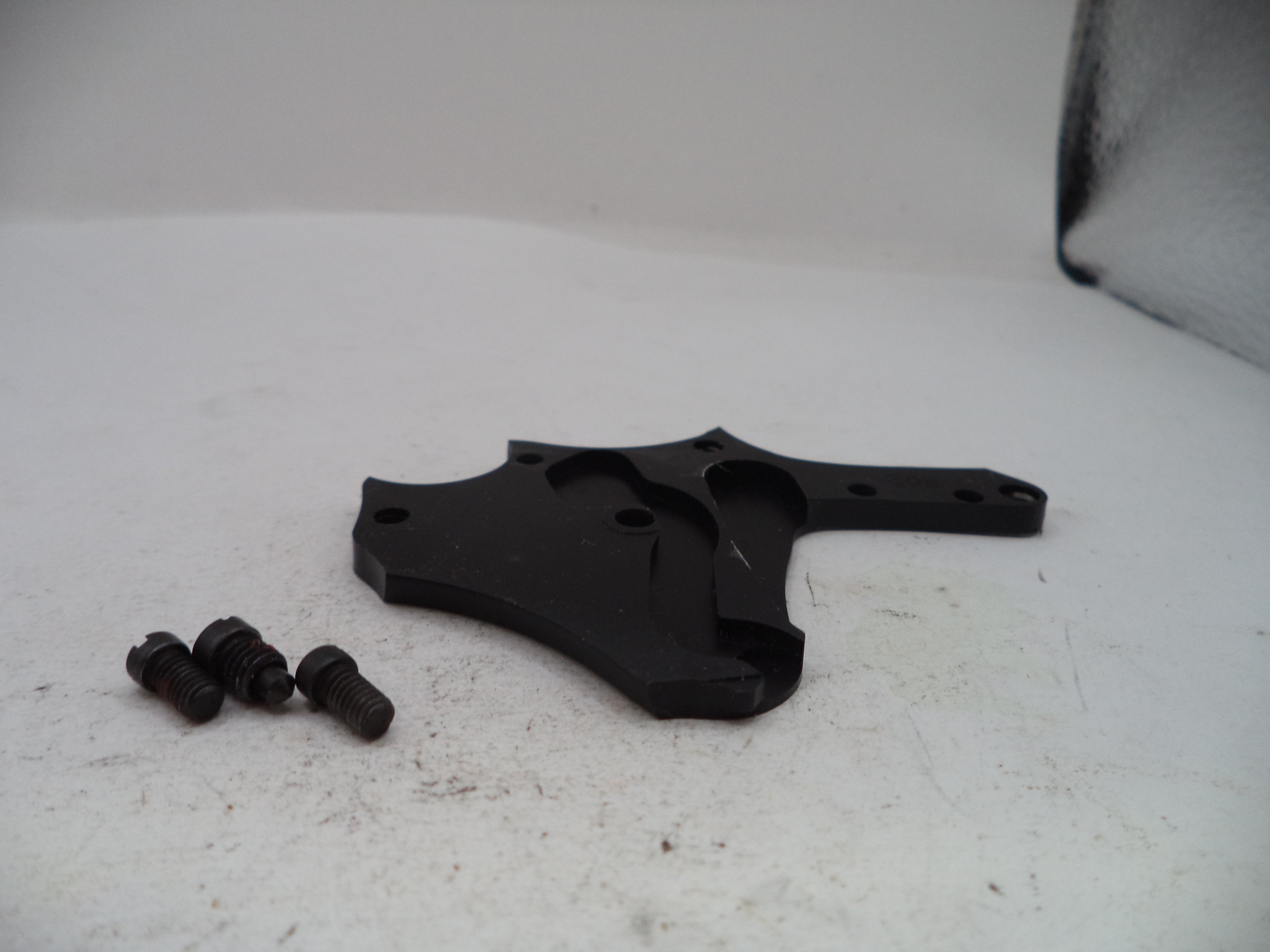 A black plastic or metal mounting bracket with three small dark screws, photographed on a white surface with a white backdrop.