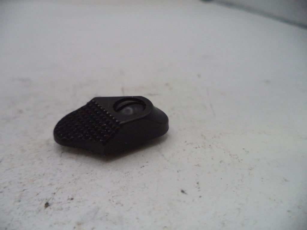 A small black plastic accessory with a textured grip and a circular cutout, resting on a dirty off-white surface.