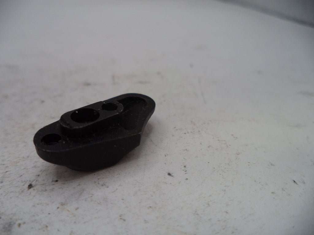 A small black plastic mechanical or automotive part with two circular holes, resting on a dirty, off-white surface.